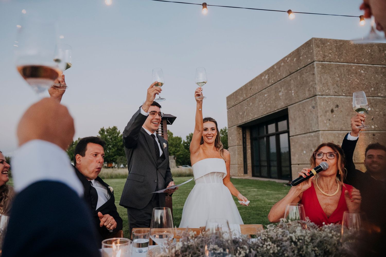 A bride and groom raising glasses in a toast with guests at an elegant outdoor wedding reception.