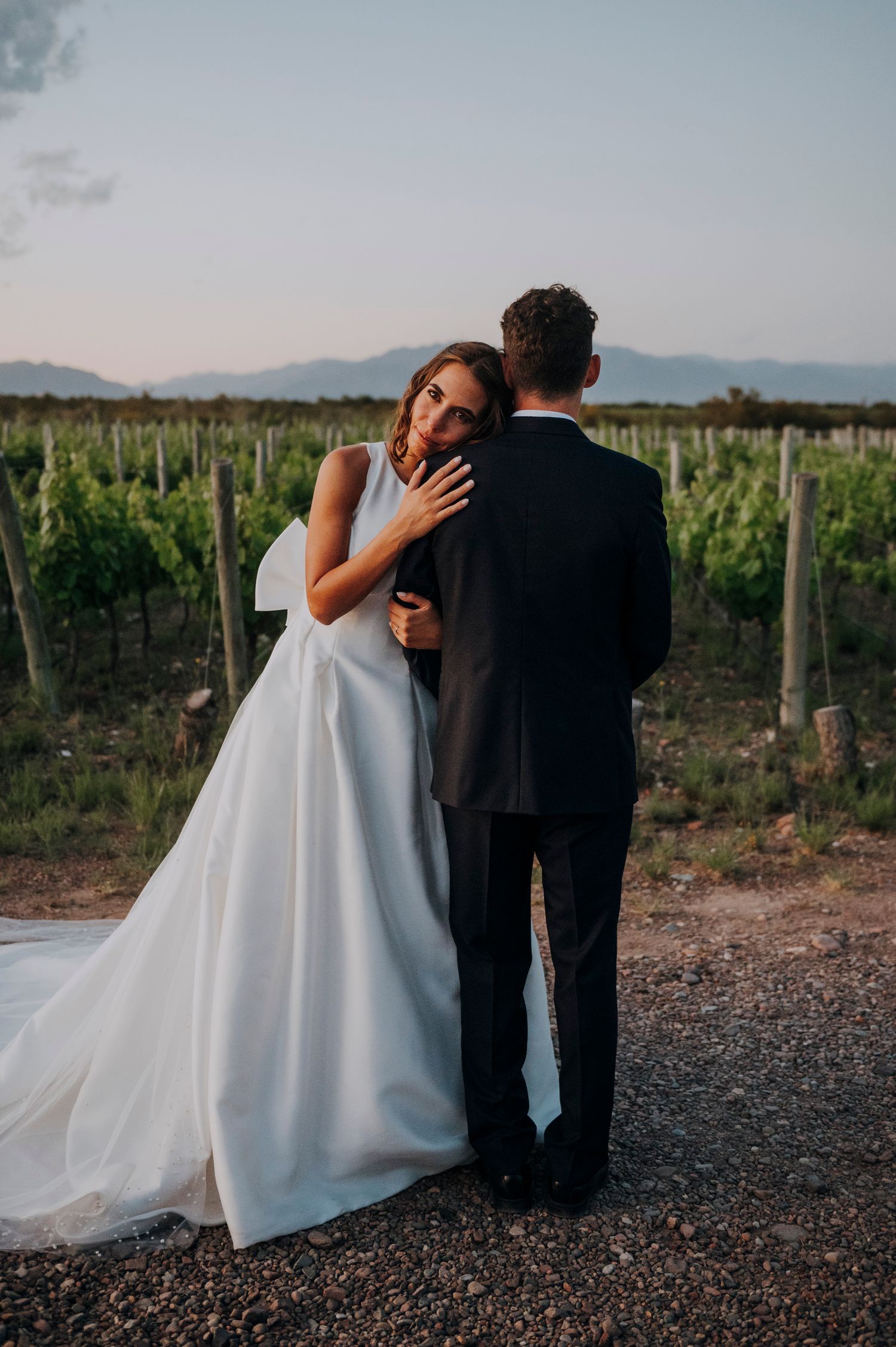 Bride and groom embracing at sunset in front of scenic vineyard landscape.