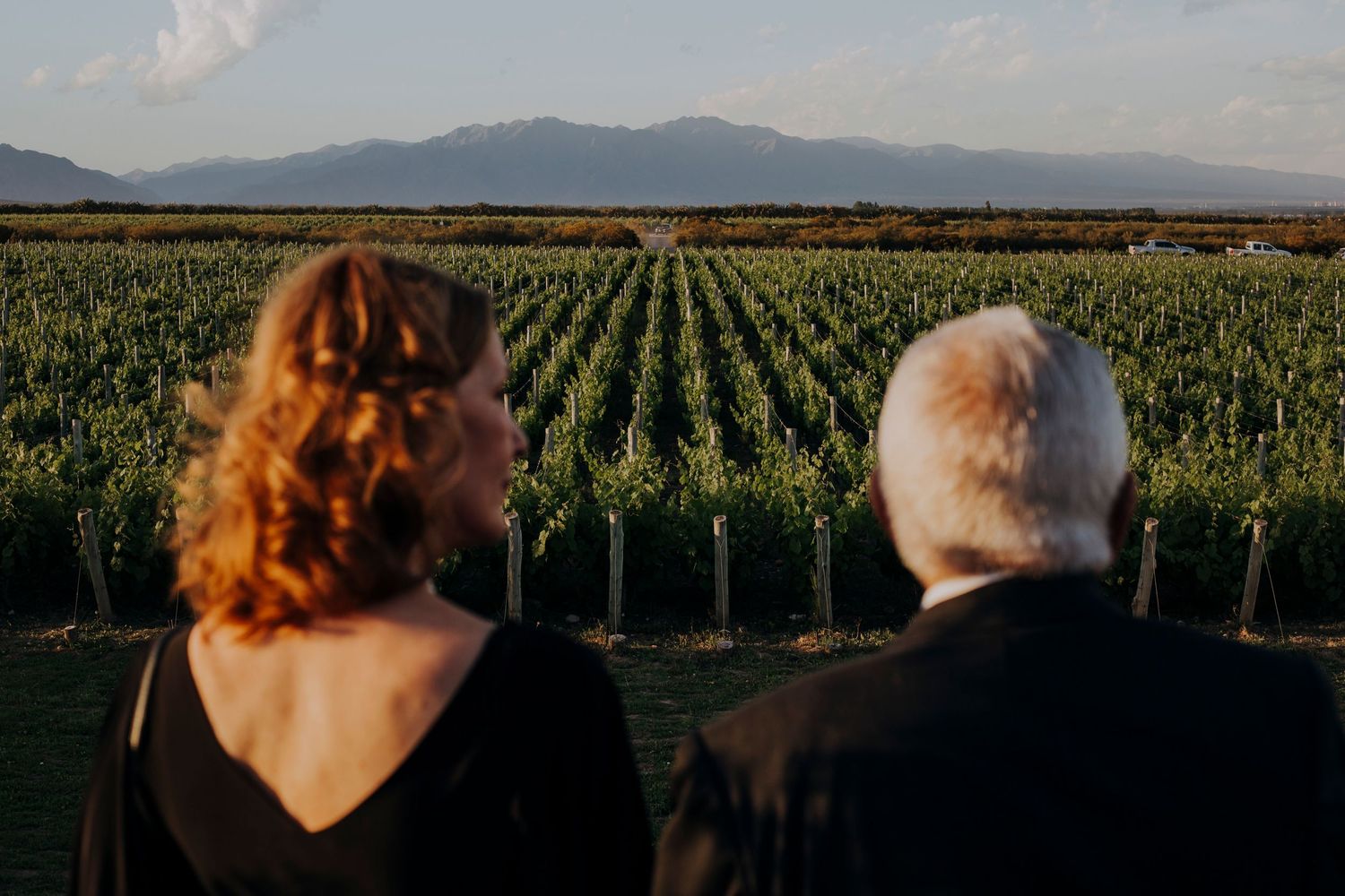 Couple in black attire admire scenic vineyard and mountain views at sunset wedding venue.