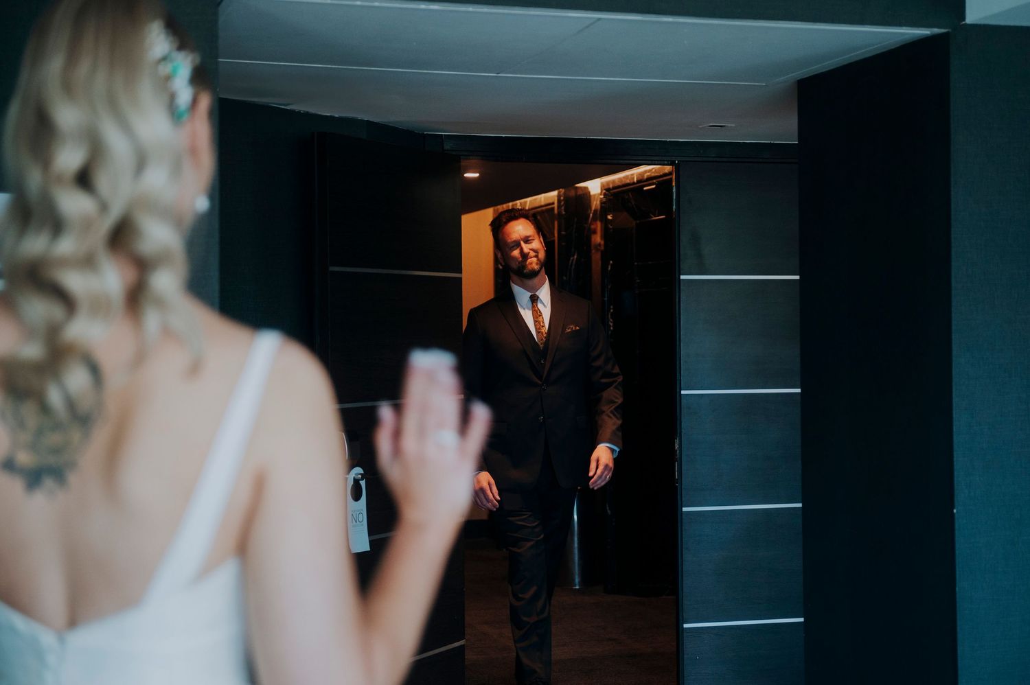 Groom in dark suit smiles at bride in white dress during emotional first look moment in elegant venue.