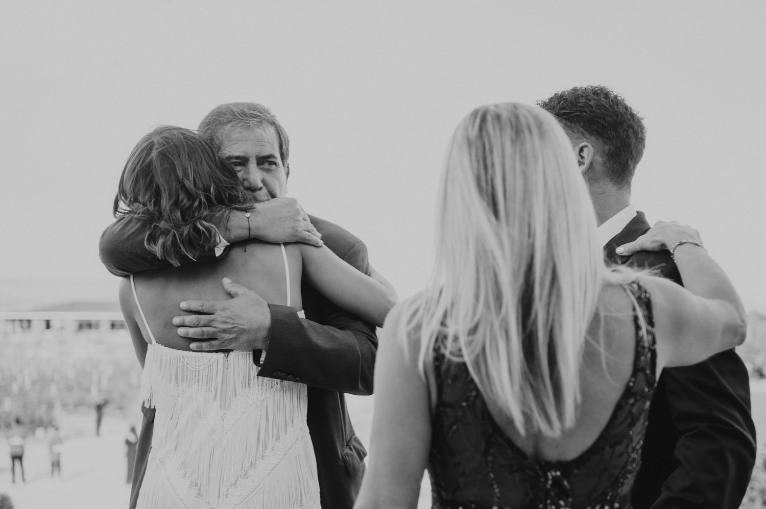 Black and white photo of couples embracing warmly at a wedding celebration outdoors.