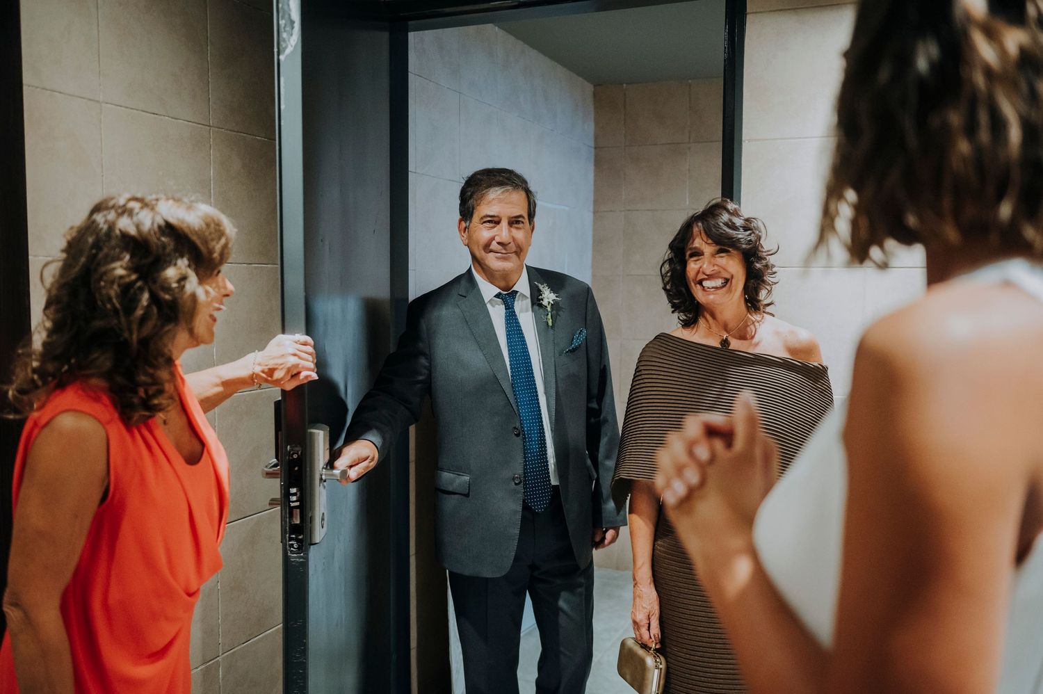 Elegant couple in formal attire greeted by guests at a wedding venue doorway.
