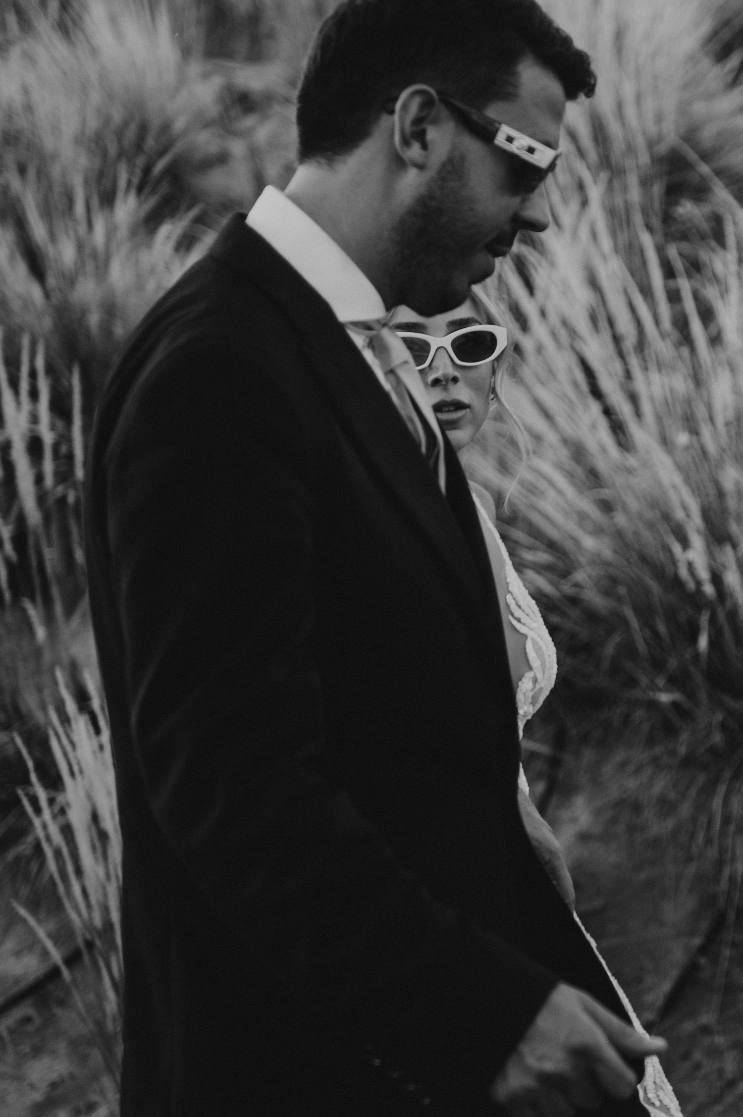 Stylish couple in black and white, groom in suit, bride in cat-eye sunglasses at wedding. Couple portrait in Mendoza.