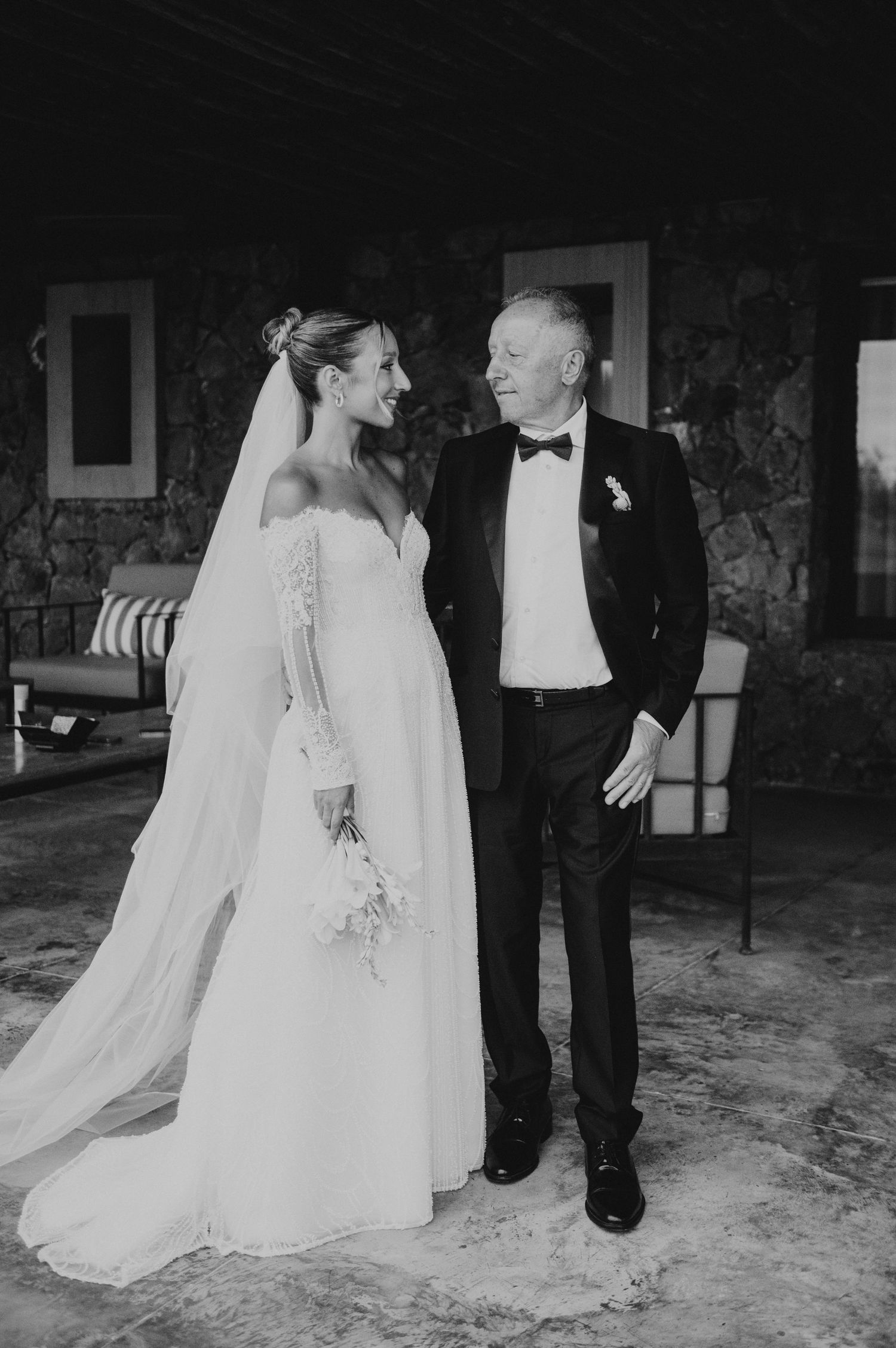 Black and white photo of smiling bride in veil and gown standing with older man in tuxedo.