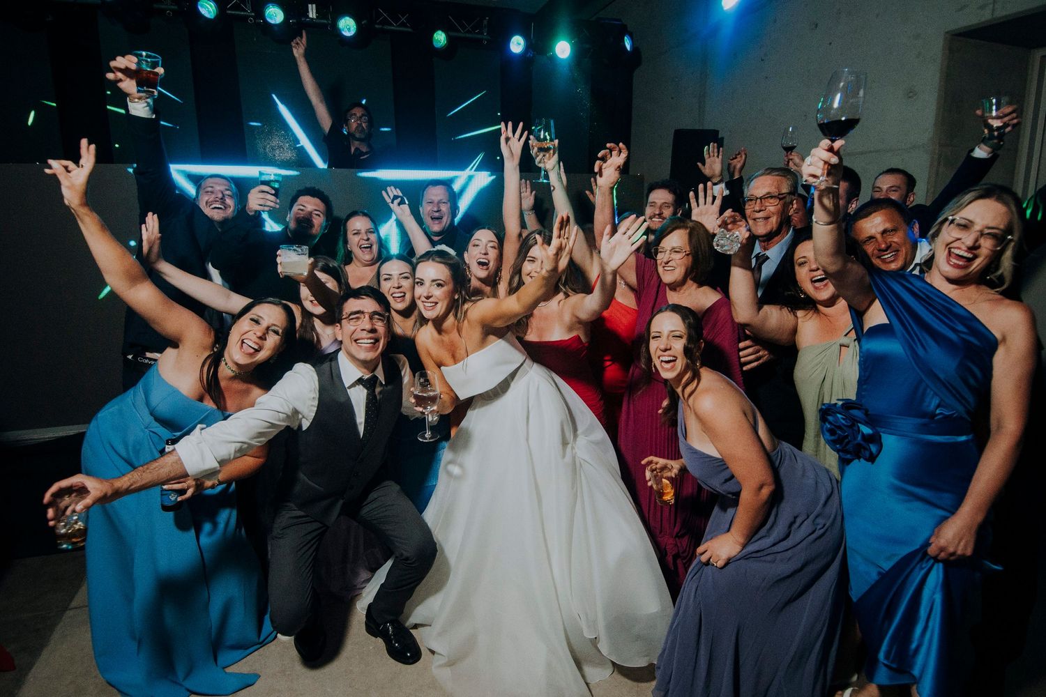 Bride groom and wedding party celebrating together in lively group photo on dance floor.