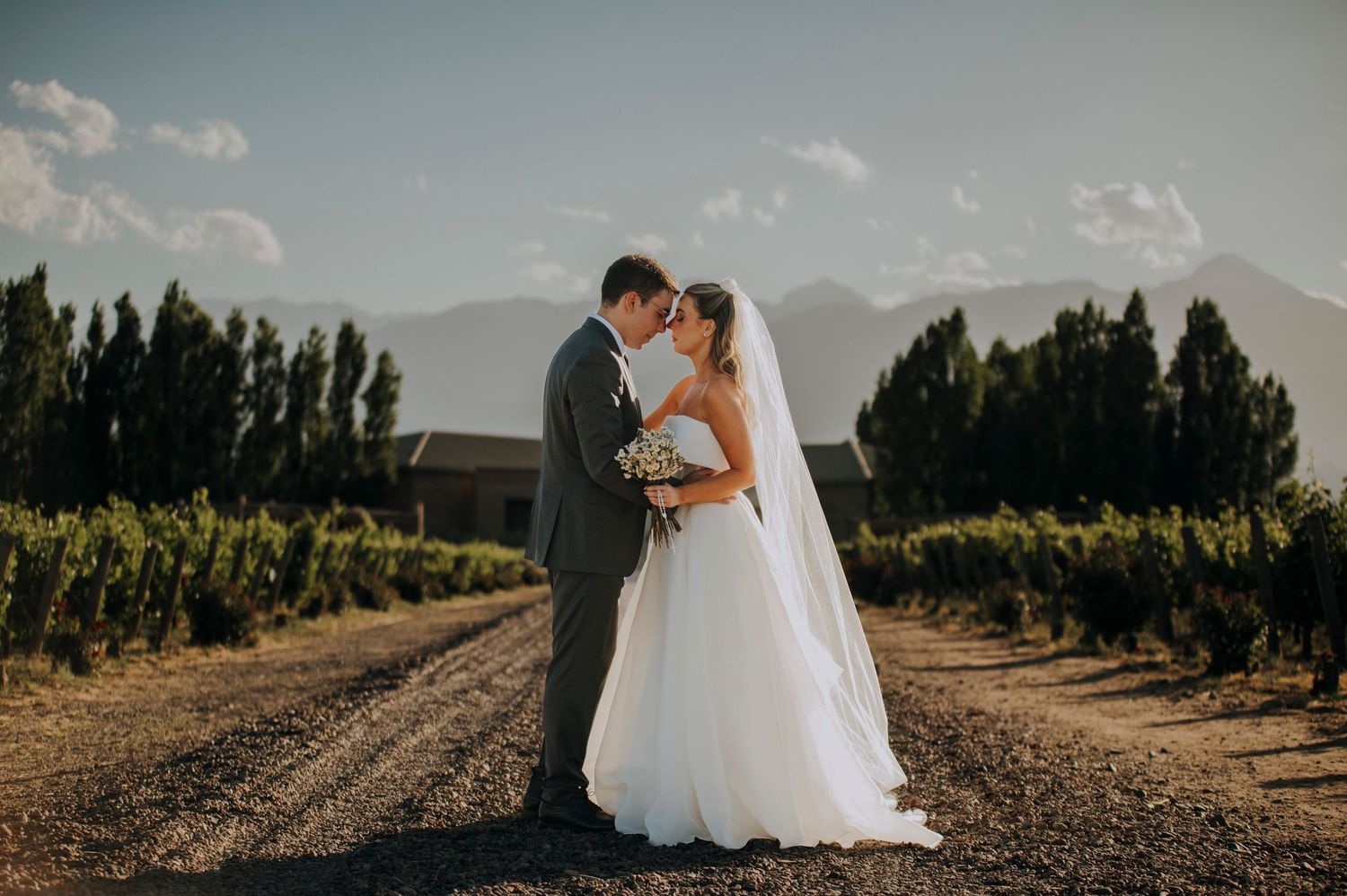 A romantic bride and groom sharing an intimate moment on a gravel path surrounded by vineyard rows.