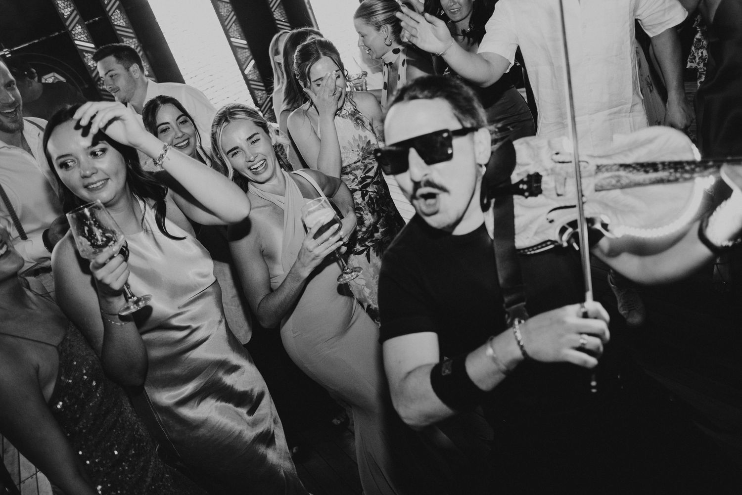 Black and white photo of people dancing and taking selfies at a lively party event.