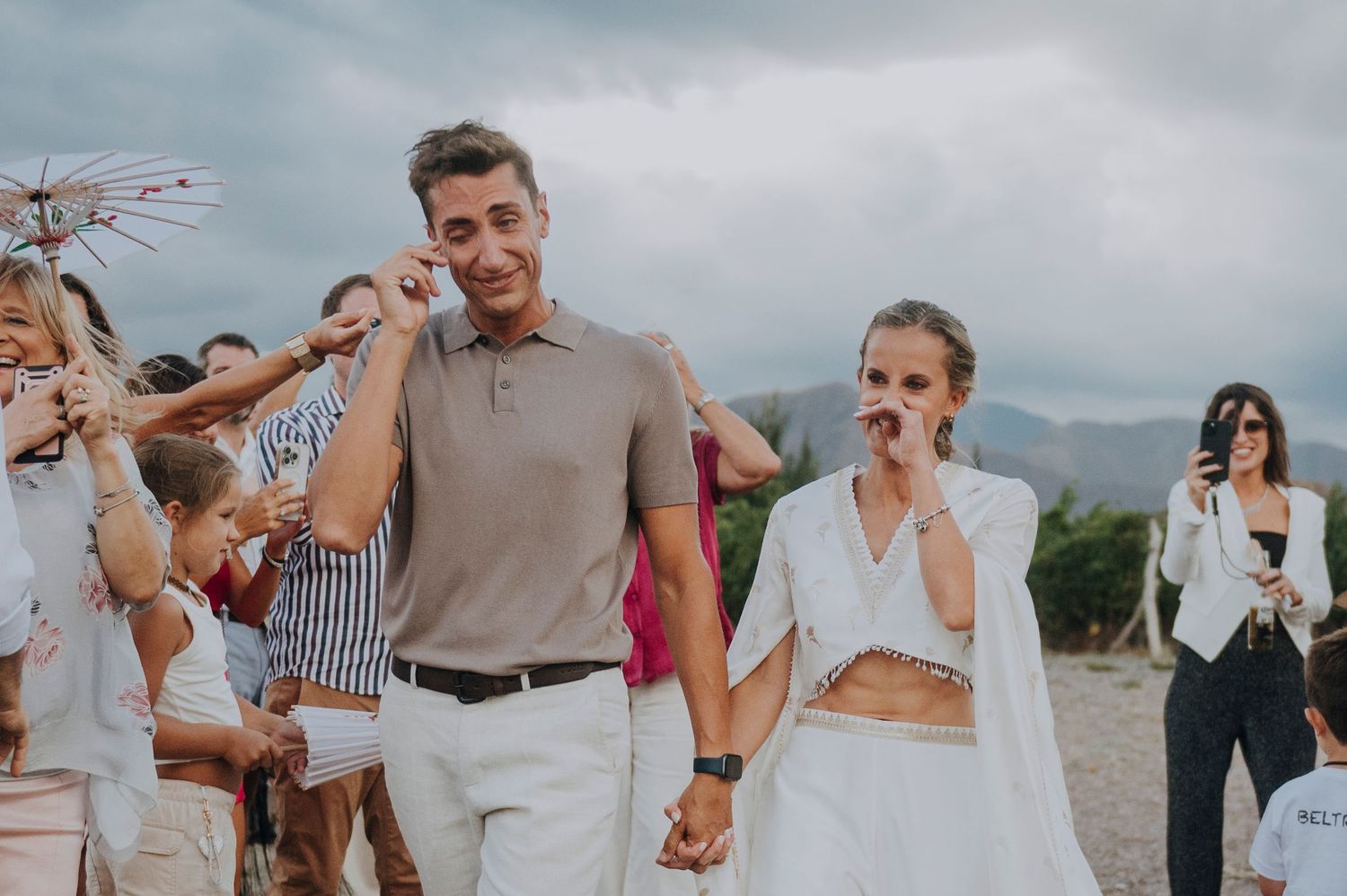 Smiling bride and groom walk hand-in-hand at outdoor wedding celebration with guests. Emotional ceremony in Mendoza.