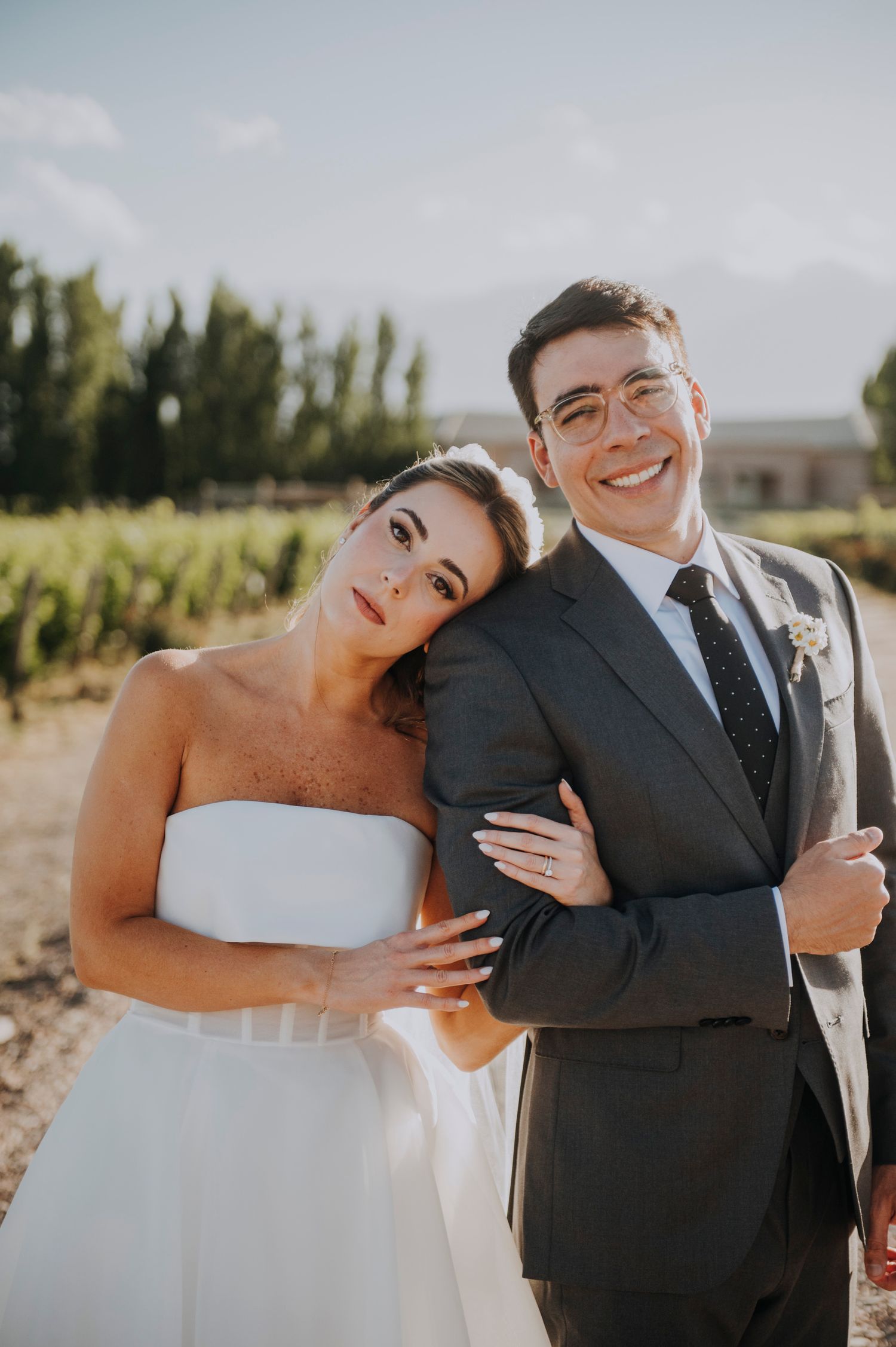 Happy bride and groom posing together at vineyard wedding, bride in strapless white gown.