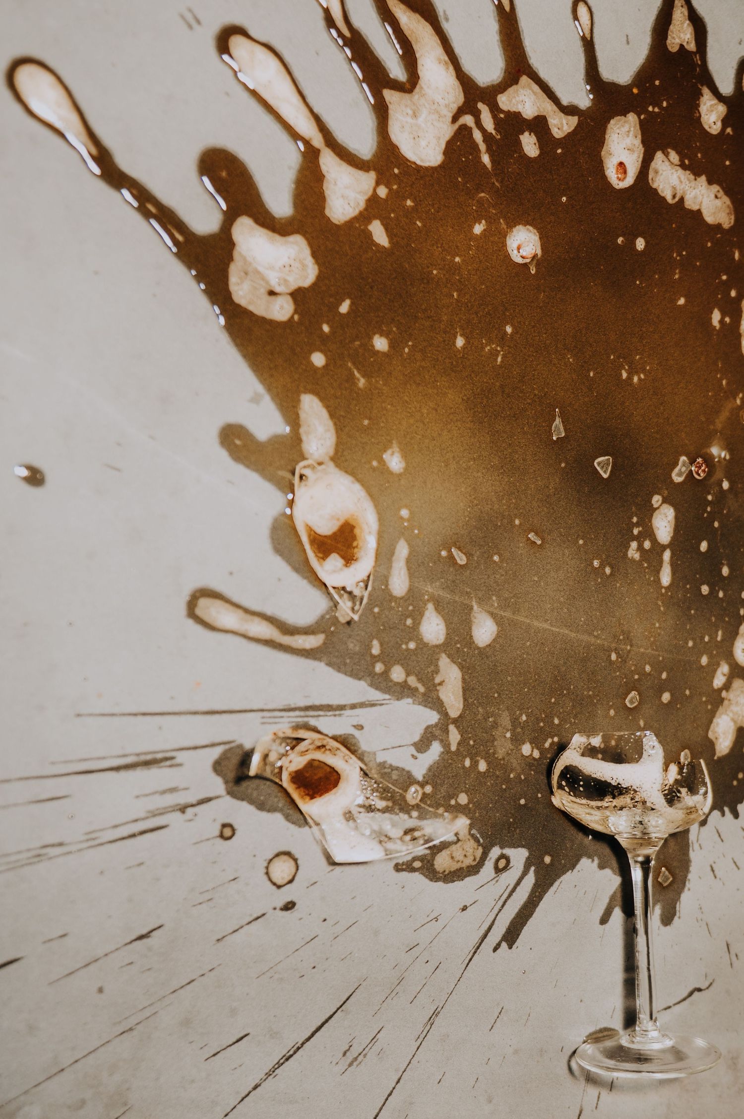Broken champagne glass with spilled wine splattered on white floor at wedding reception.