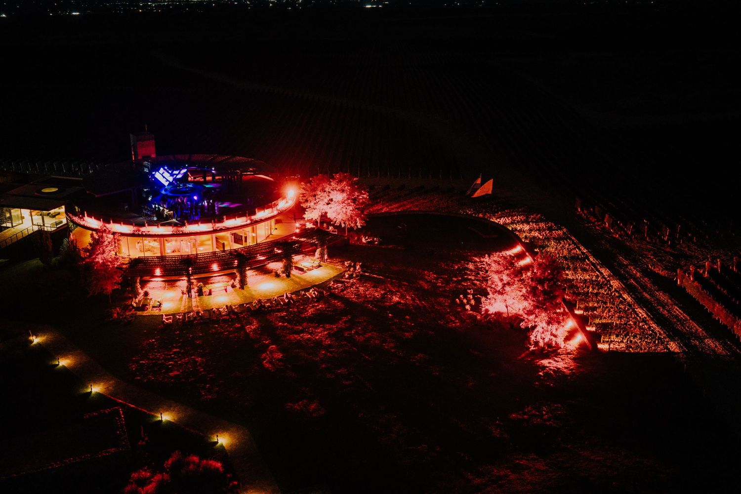 Aerial night view of outdoor wedding venue illuminated by red fireworks and colorful stage lighting.