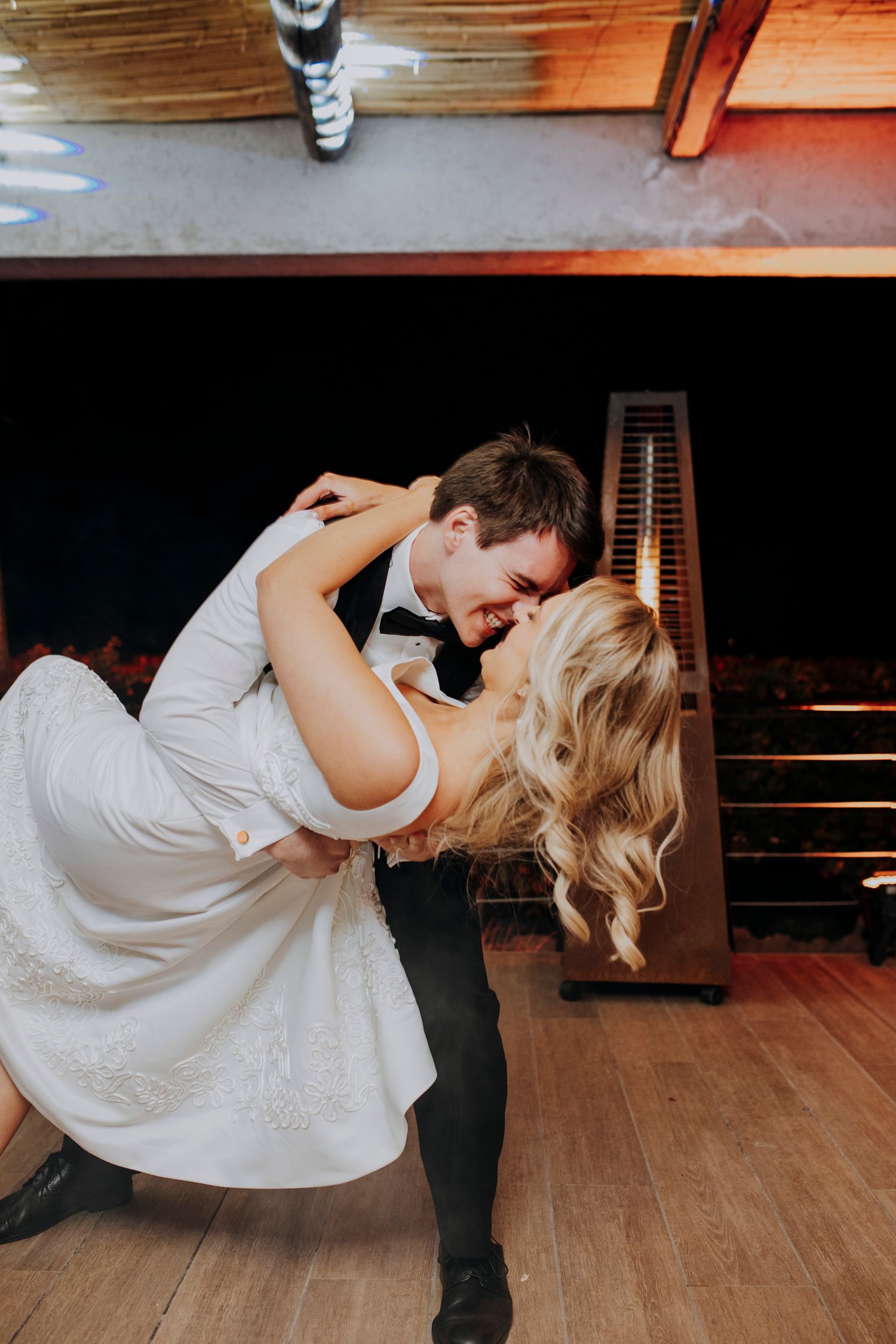 Groom dips bride in romantic first dance moment at dimly lit wedding reception venue.