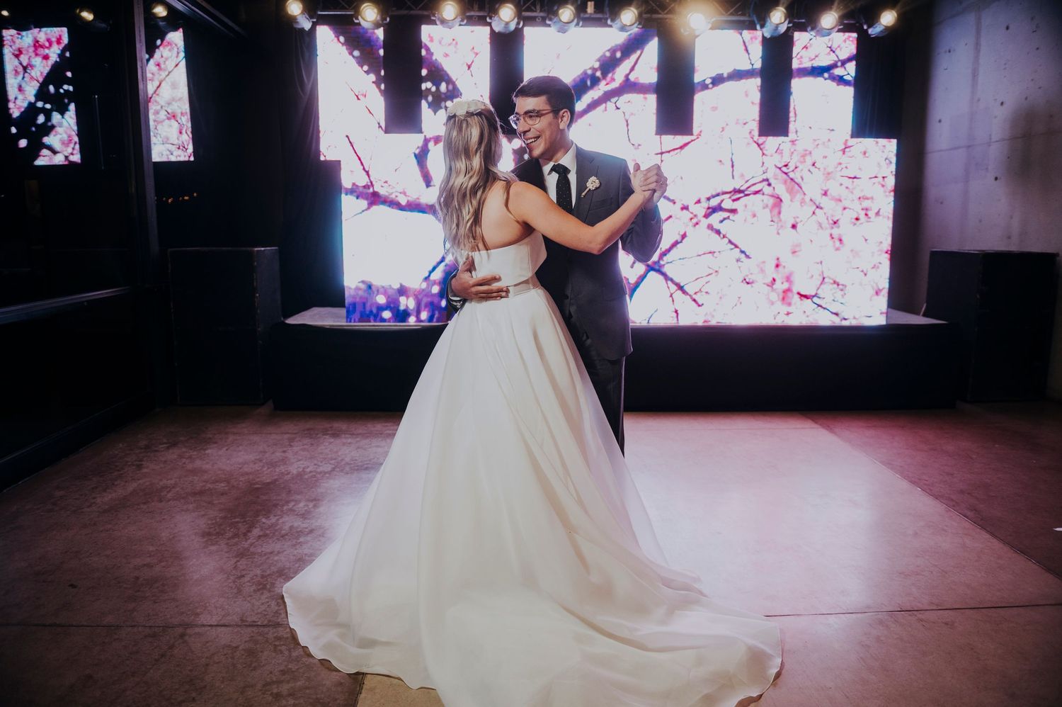 Bride and groom sharing a romantic first dance in front of a floral LED backdrop at their reception.