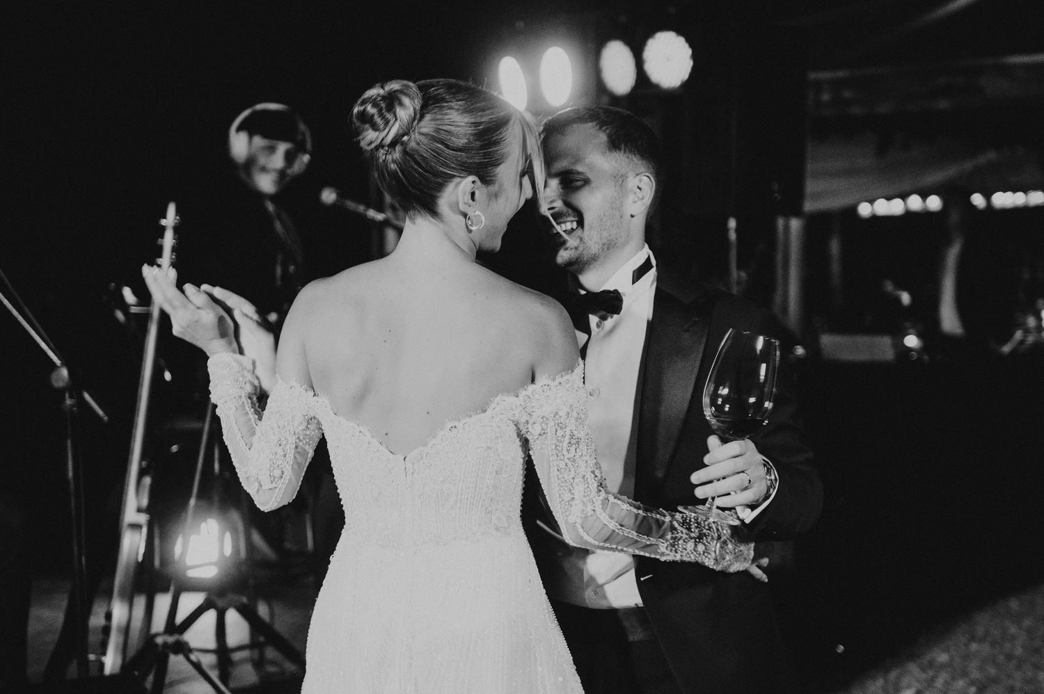 Black and white photo of a bride and groom sharing a romantic dance at their wedding reception with a live band.
