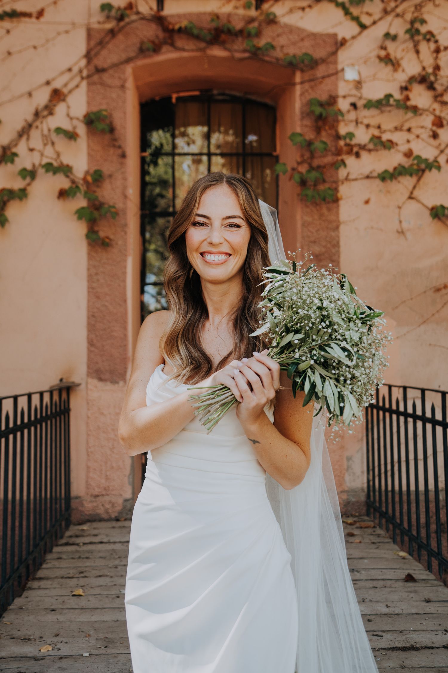 Radiant bride in white gown holds wildflower bouquet outside pink stone building in mendoza