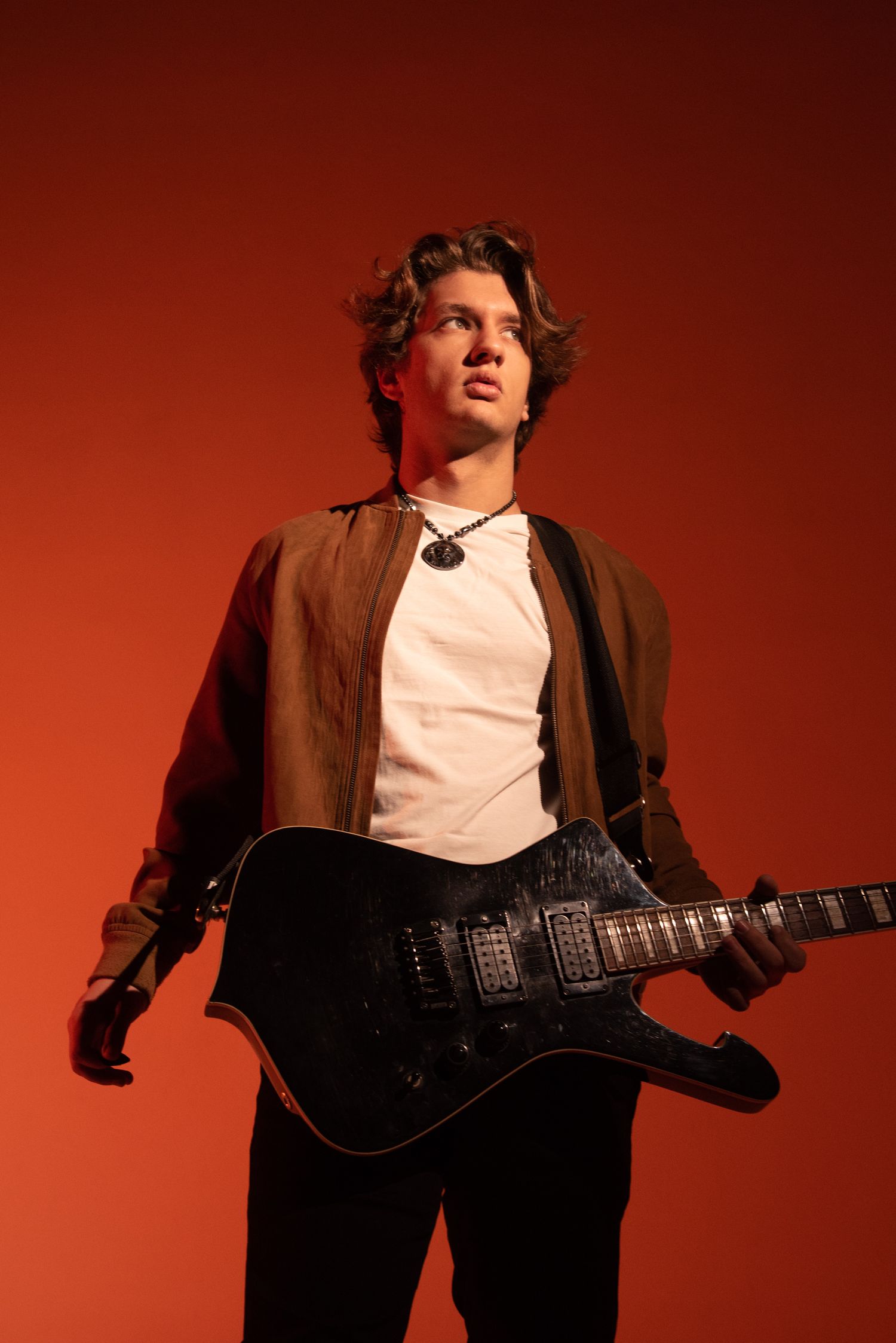 cite Young male guitarist holding a black electric guitar against a red background