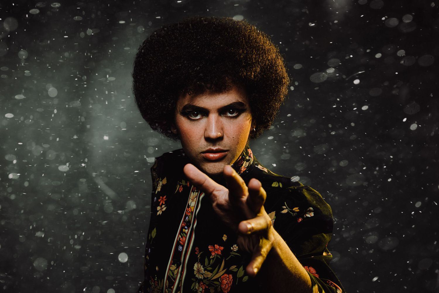 Fierce young person with afro hairstyle reaching toward camera in snowy bokeh background.