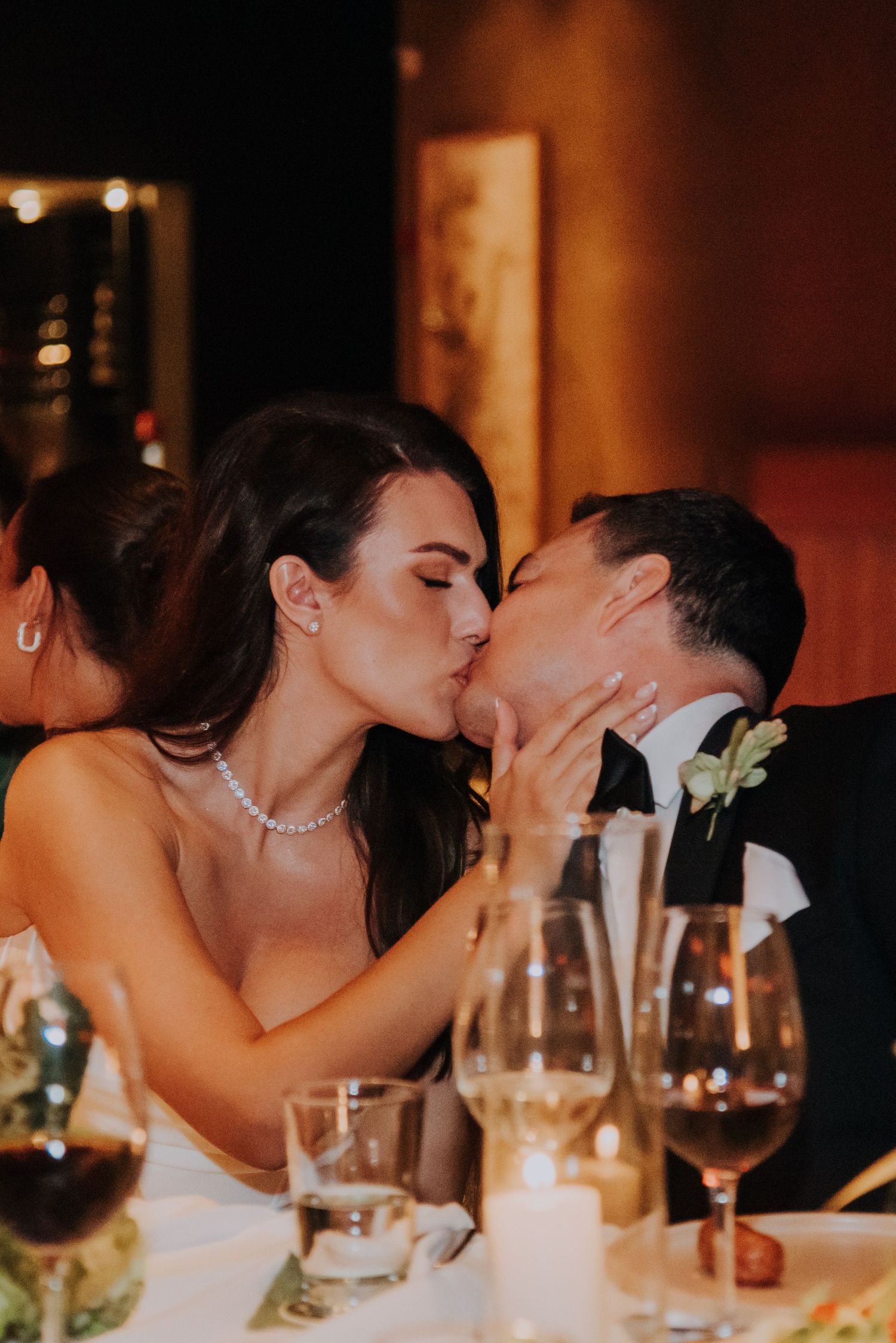 Bride and groom share a romantic kiss at candlelit wedding reception dinner table.