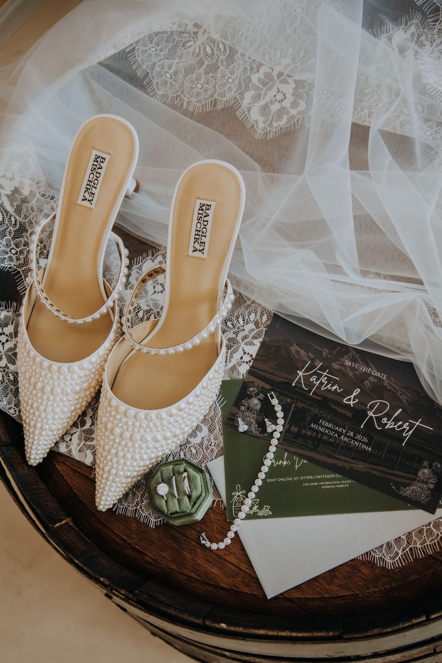 Pearl-embellished Badgley Mischka bridal heels displayed with green and white wedding invitations and delicate veil.