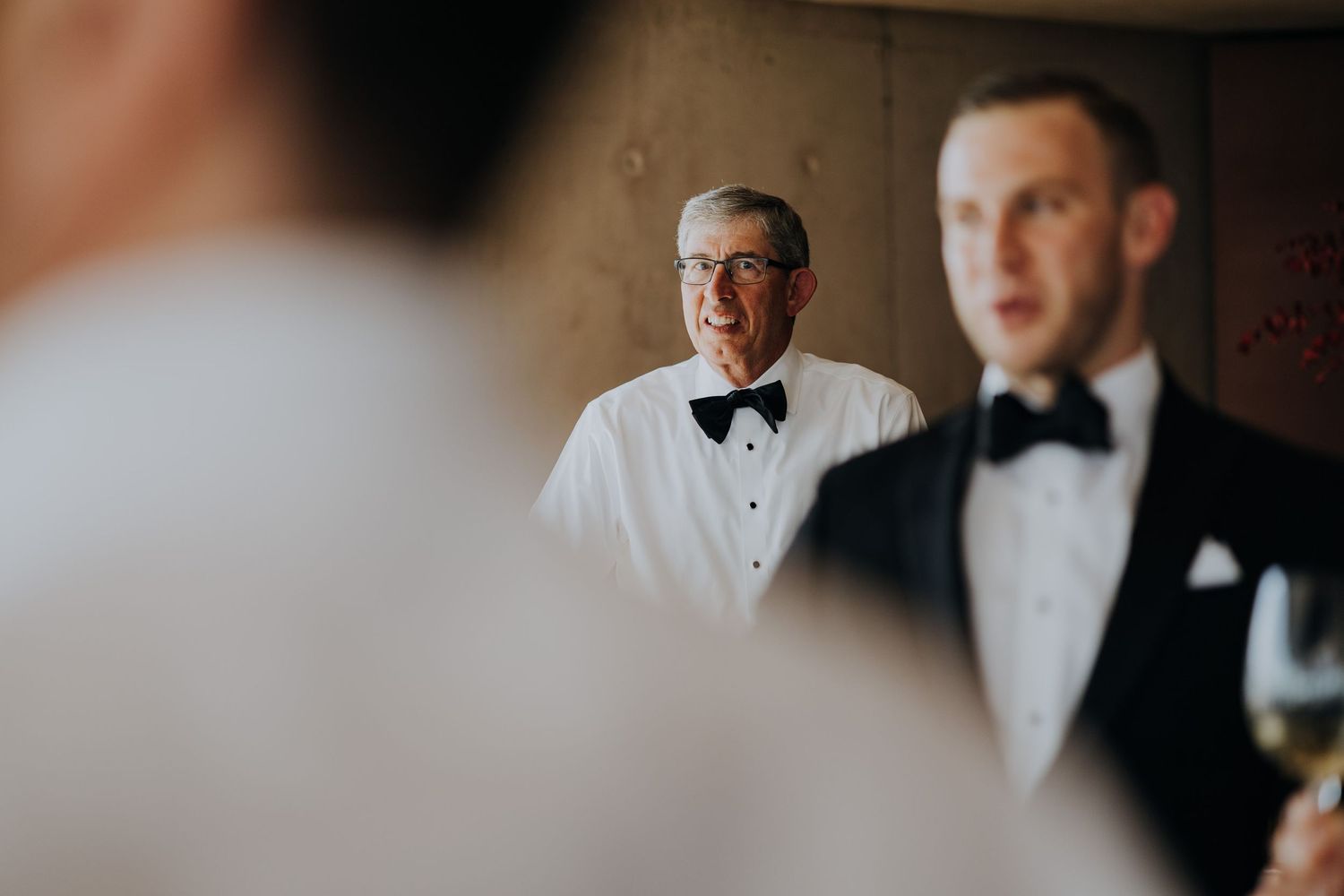 Two men in black bow ties and tuxedos stand at a formal wedding reception event.