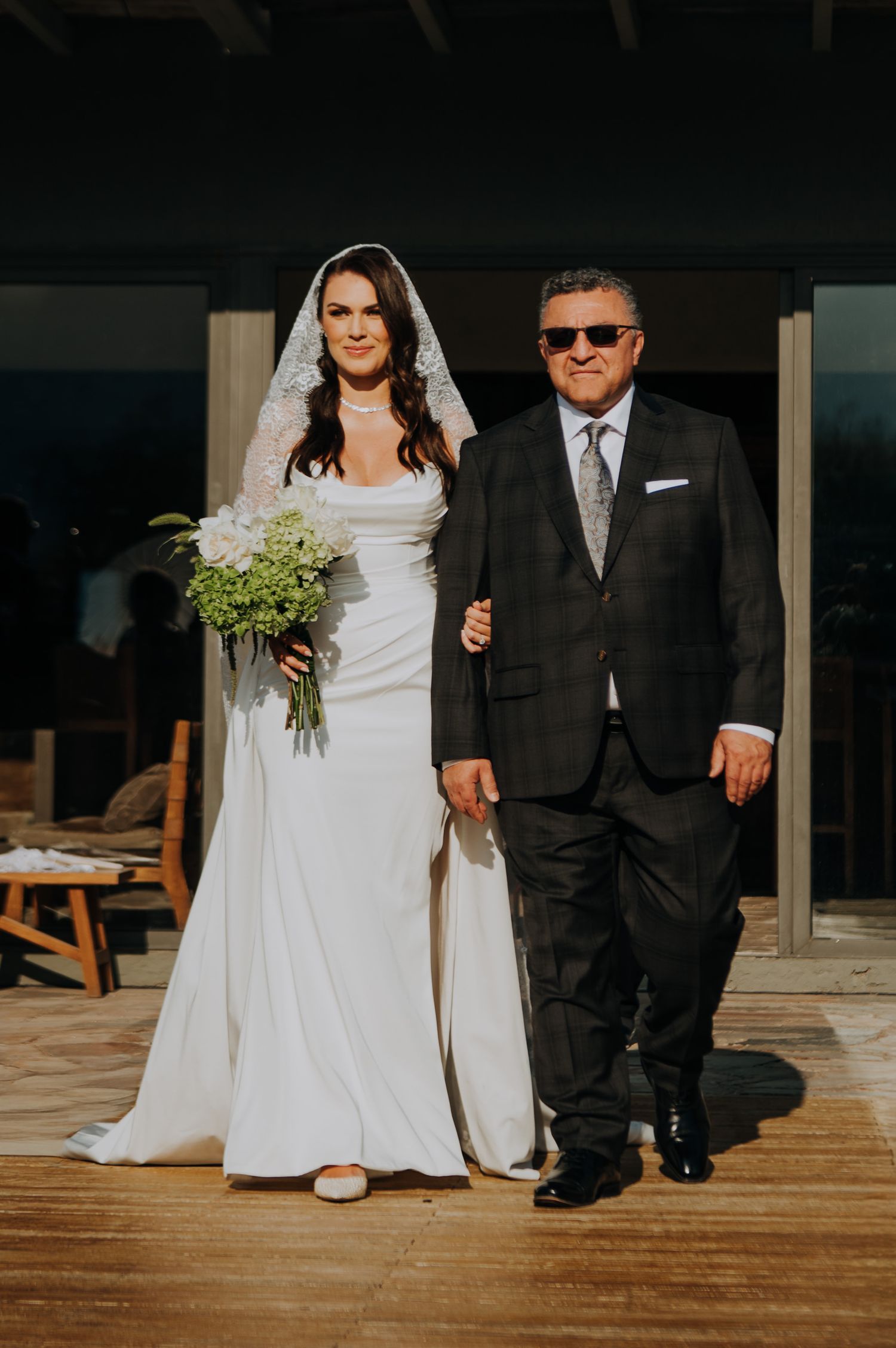 Bride in elegant white gown and veil walking with father during wedding ceremony.