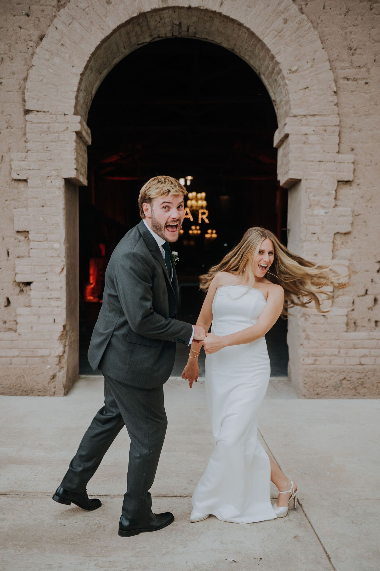 Excited bride and groom laughing outside a brick archway venue entrance  in Mendoza, Argentina.
