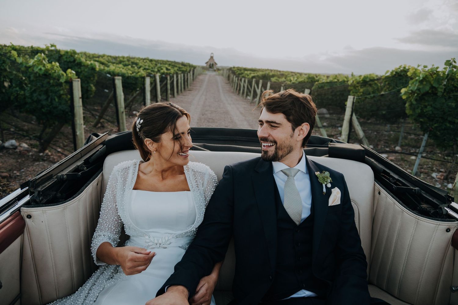 Bride and groom sharing a romantic moment in a vintage convertible through vineyard  in Mendoza, Argentina.