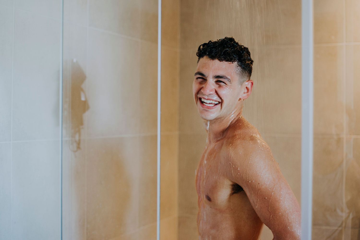 Smiling shirtless groom getting ready in shower on wedding morning.