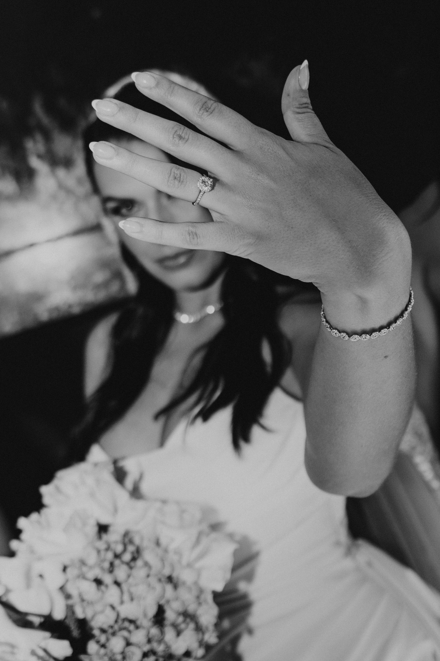 Black and white close-up of bride showing diamond engagement ring and bracelet at wedding.