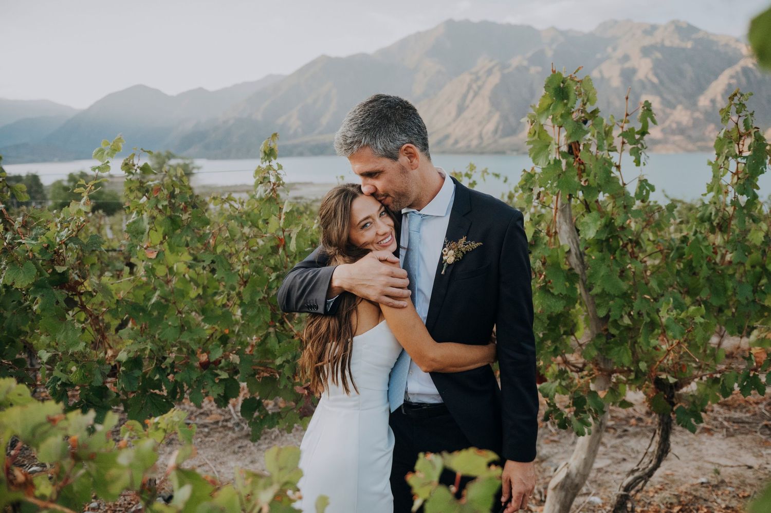 Couple embracing in a vineyard with mountain lake views on their wedding day.