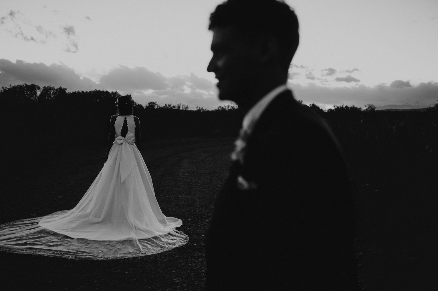 Romantic black and white silhouette of bride in flowing gown and groom at sunset.