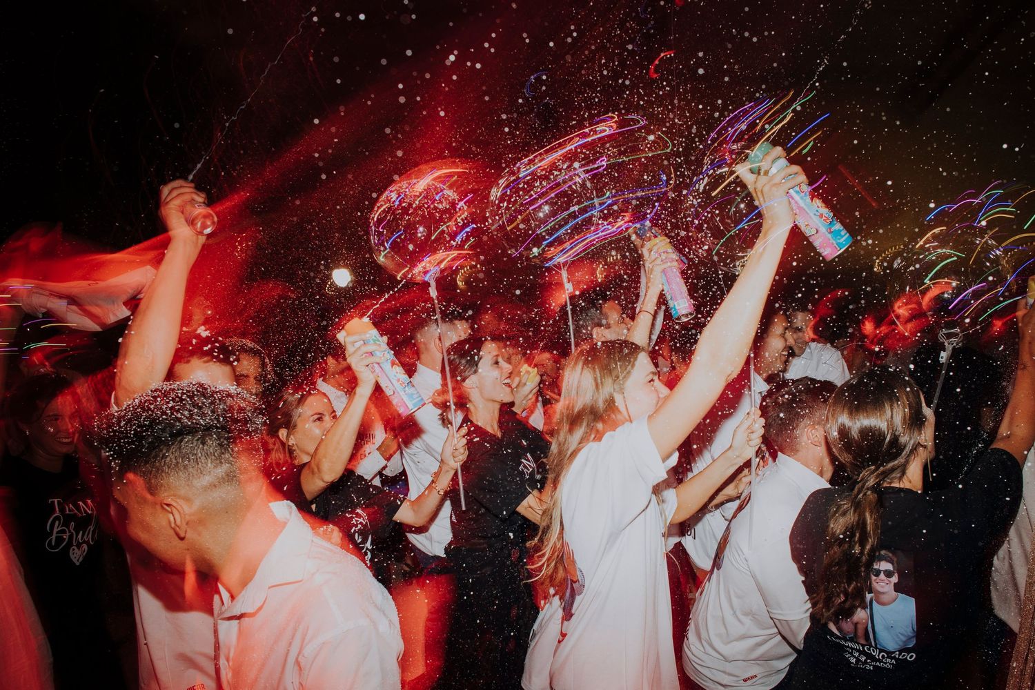 Wedding guests celebrate with confetti, balloons, and light-up wands at a festive reception party.