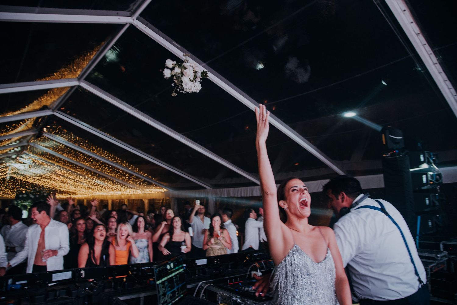 Bride tossing bouquet to excited crowd at glittering indoor wedding reception.