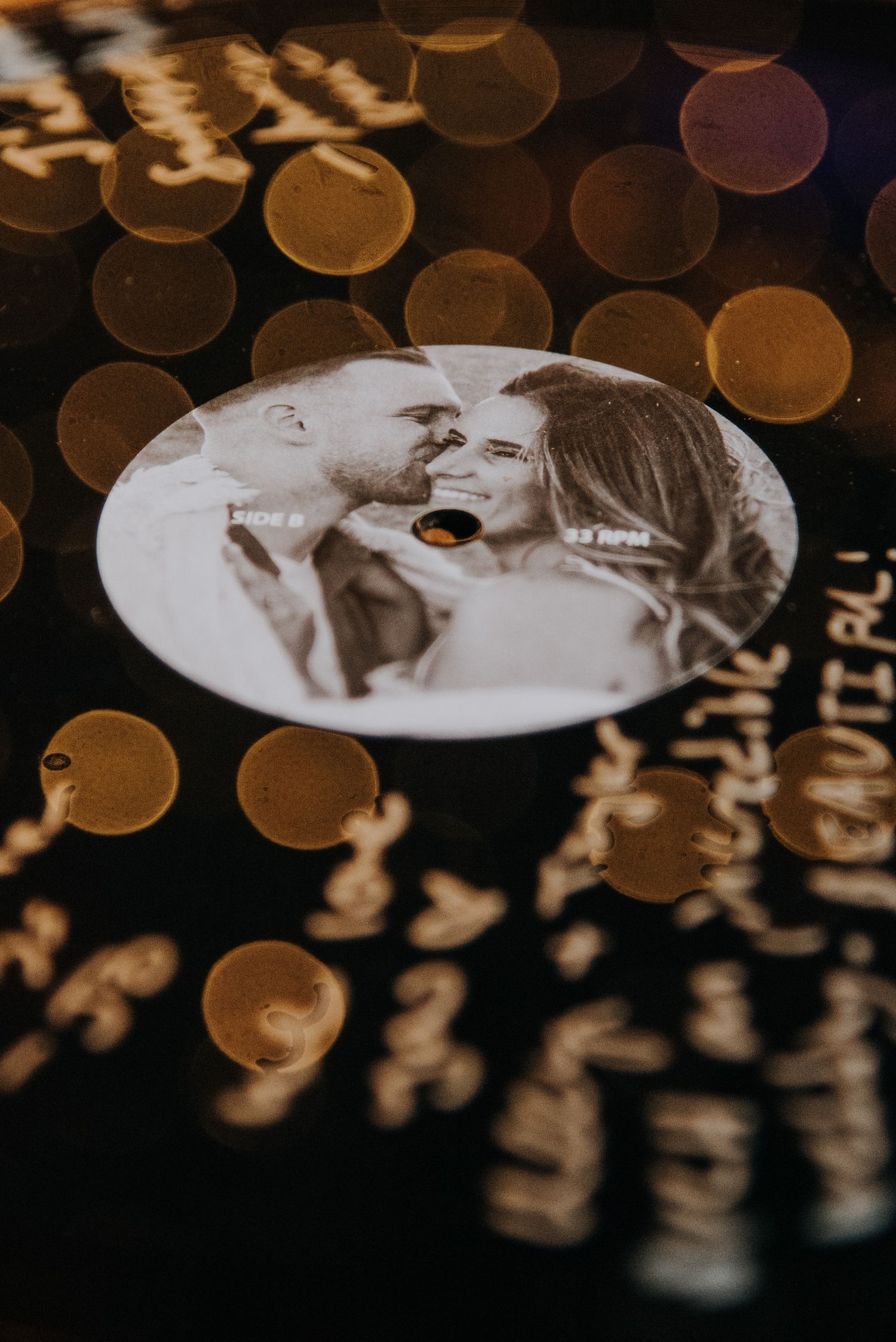 Custom vinyl record wedding favor featuring a couple's photo, surrounded by golden bokeh lights.