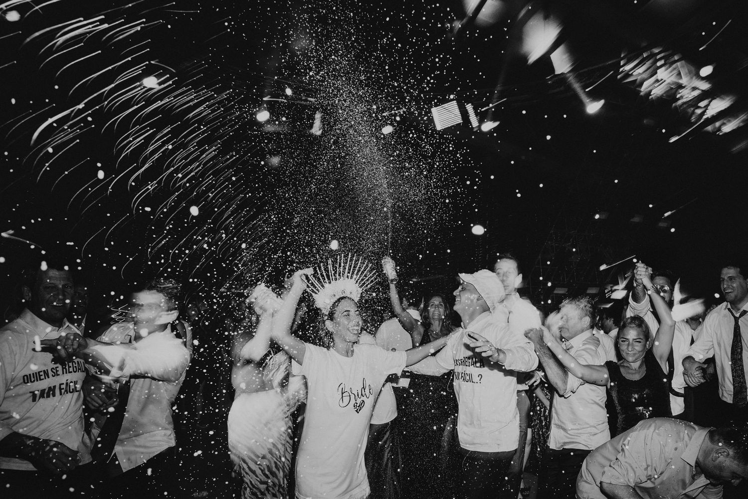 Black and white photo of wedding guests dancing with confetti at night celebration.