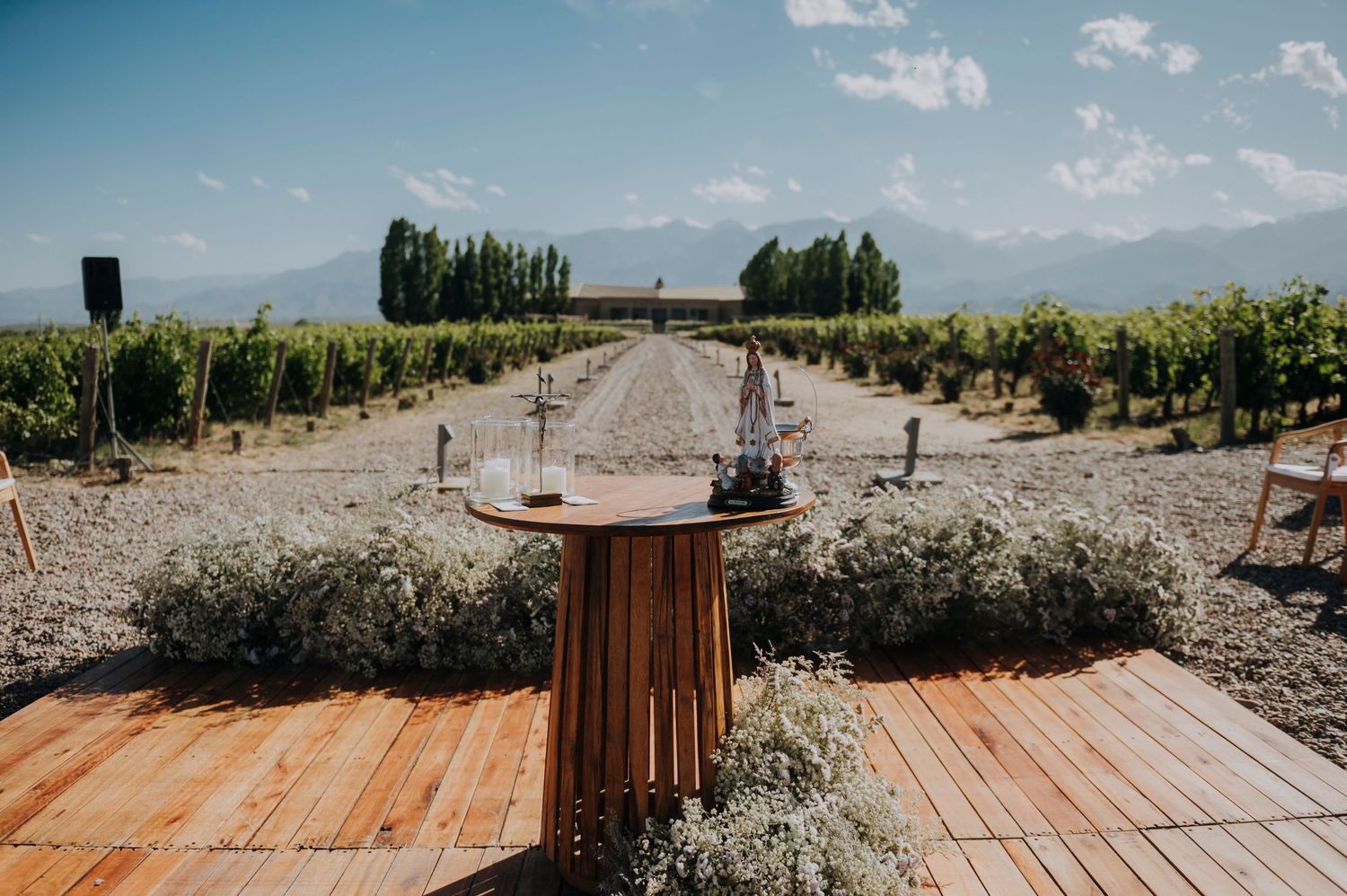 Elegant vineyard wedding venue with wooden deck, floral arrangements, and mountain backdrop under blue sky.