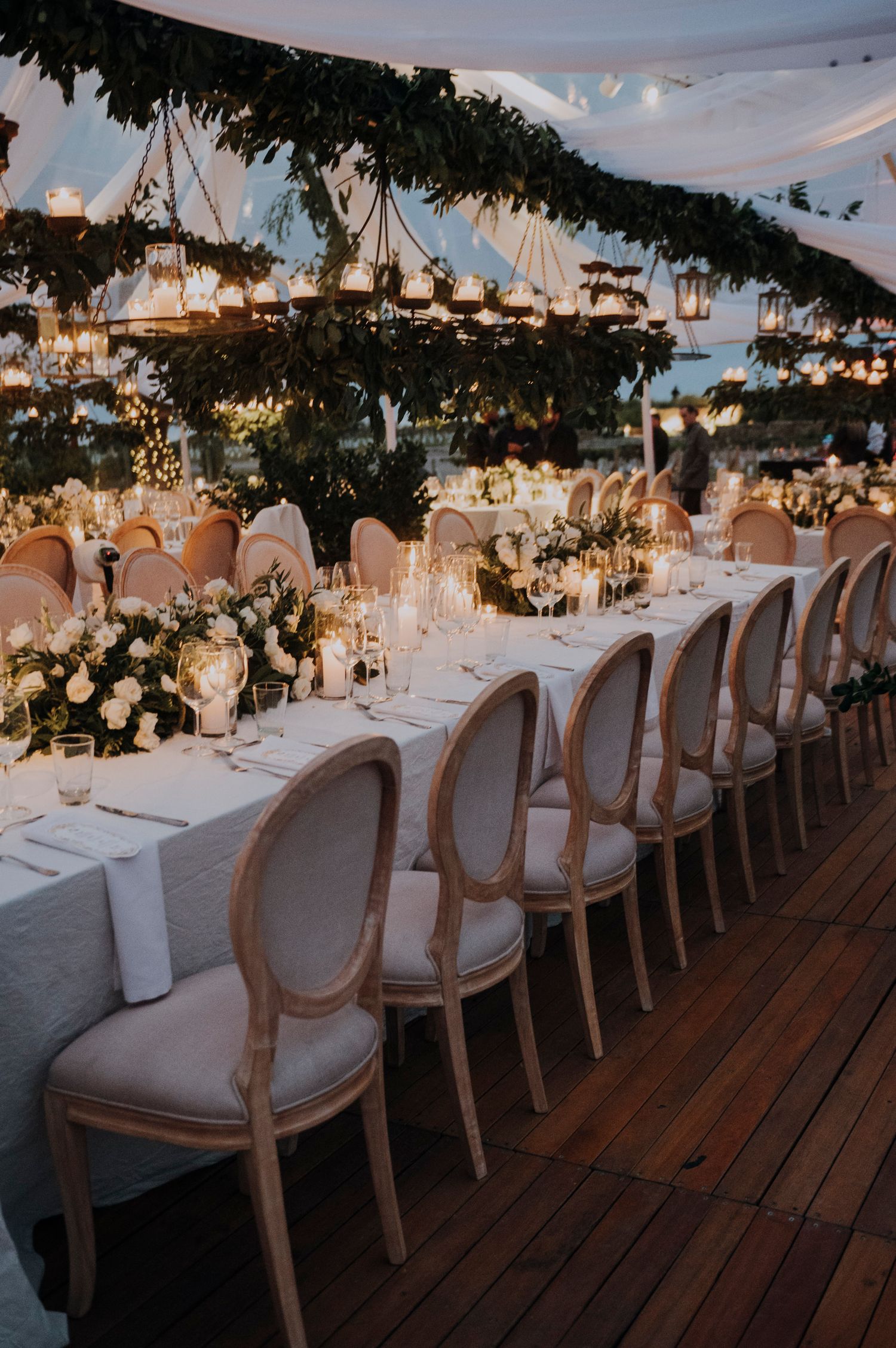 Elegant wedding reception with long tables, Louis XVI chairs, greenery, and hanging lanterns.