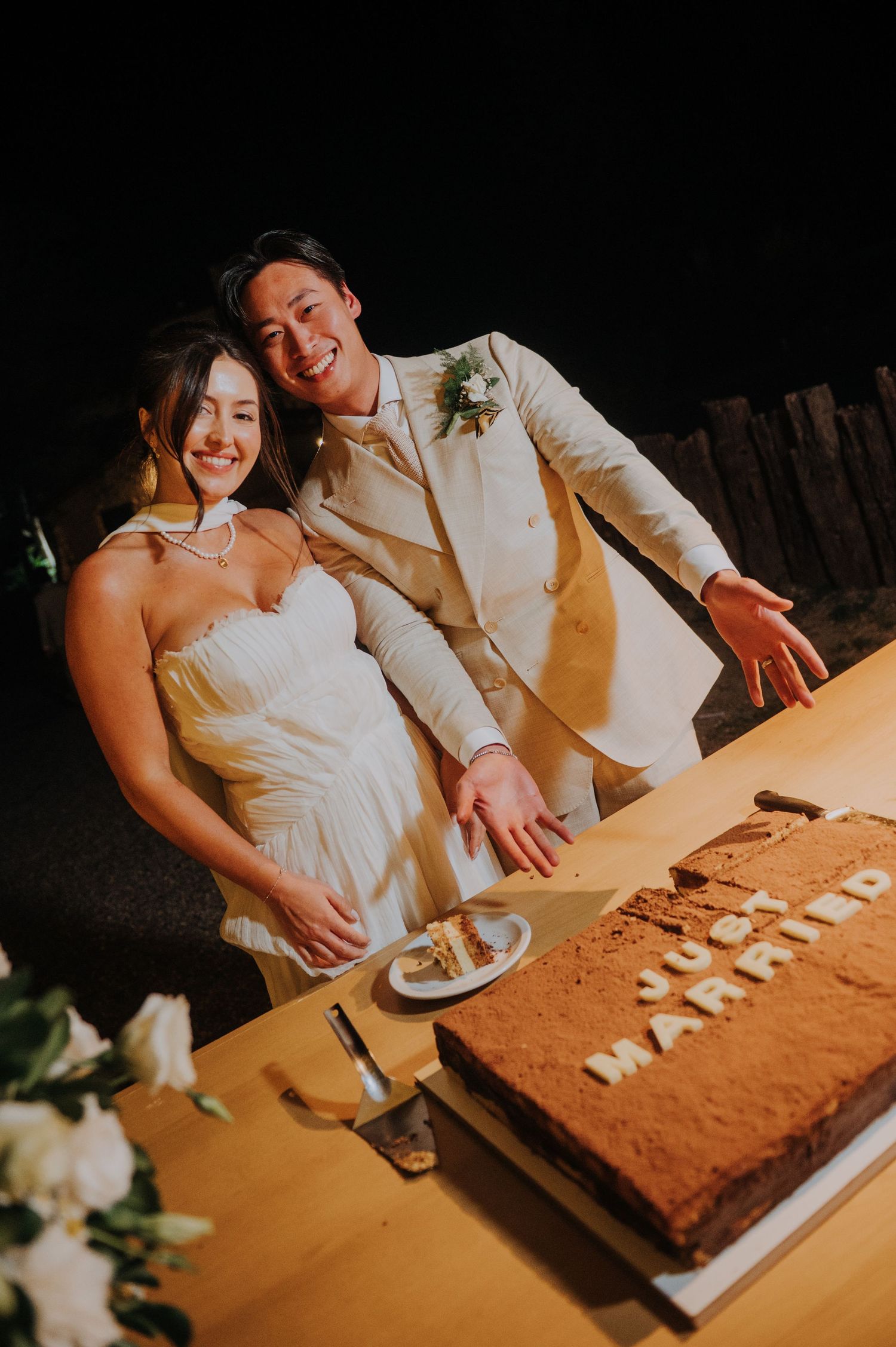 Newlyweds smiling while cutting wedding cake inscribed with just married at reception.