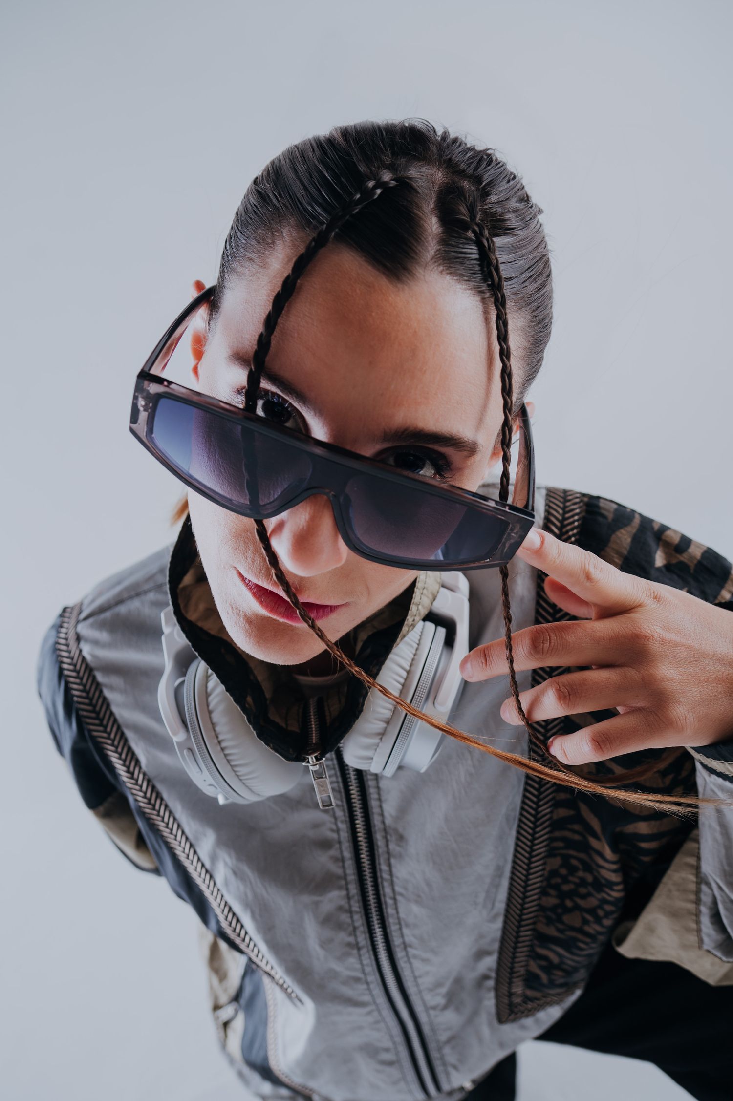 FEFI BALACCO Fashion portrait of a woman with braids pulling down oversized sunglasses wearing a silver jacket.