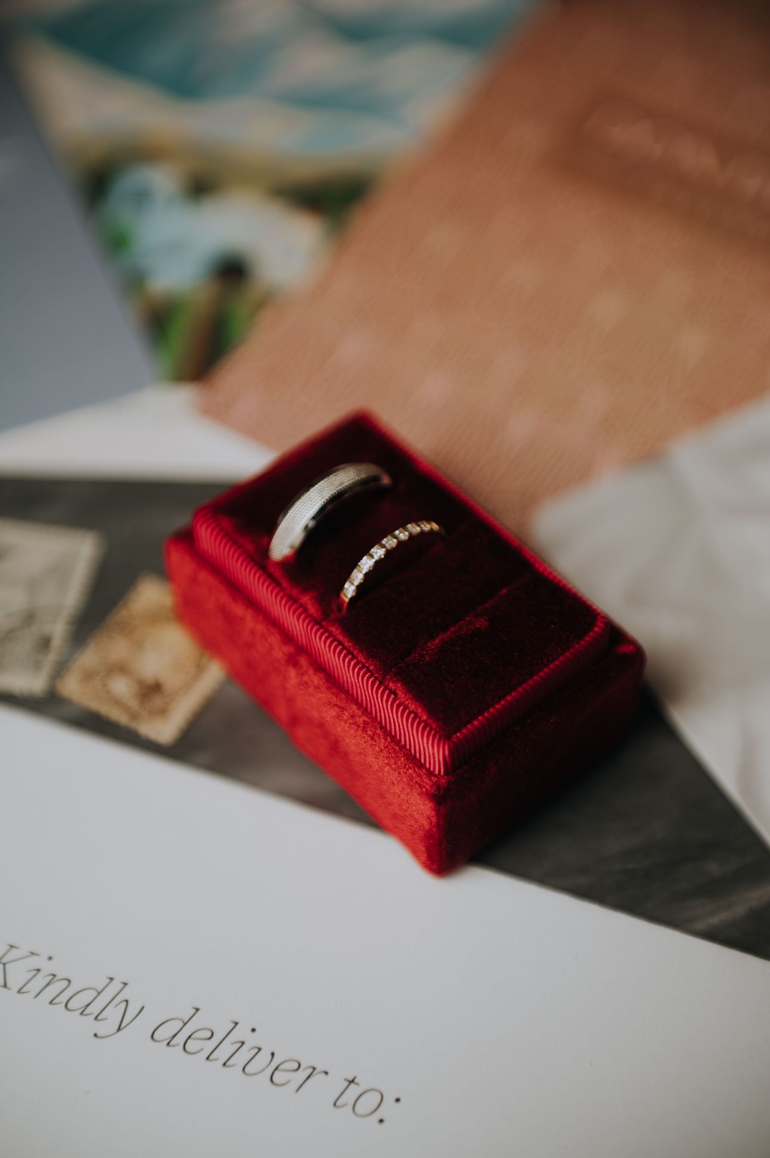 Two silver wedding bands displayed in a red velvet ring box on top of wedding stationery.