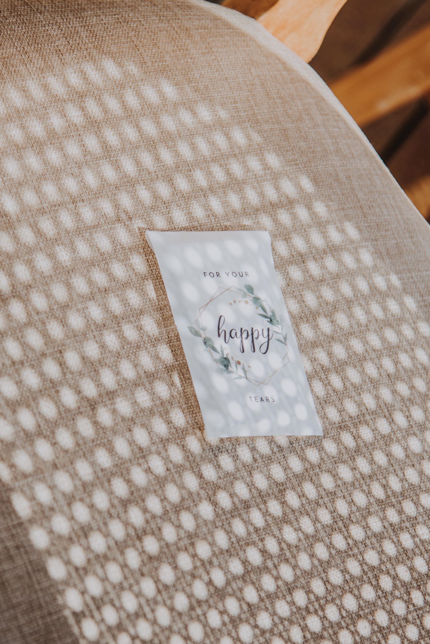 Wedding card reading happy placed on textured linen chair with soft dappled sunlight.