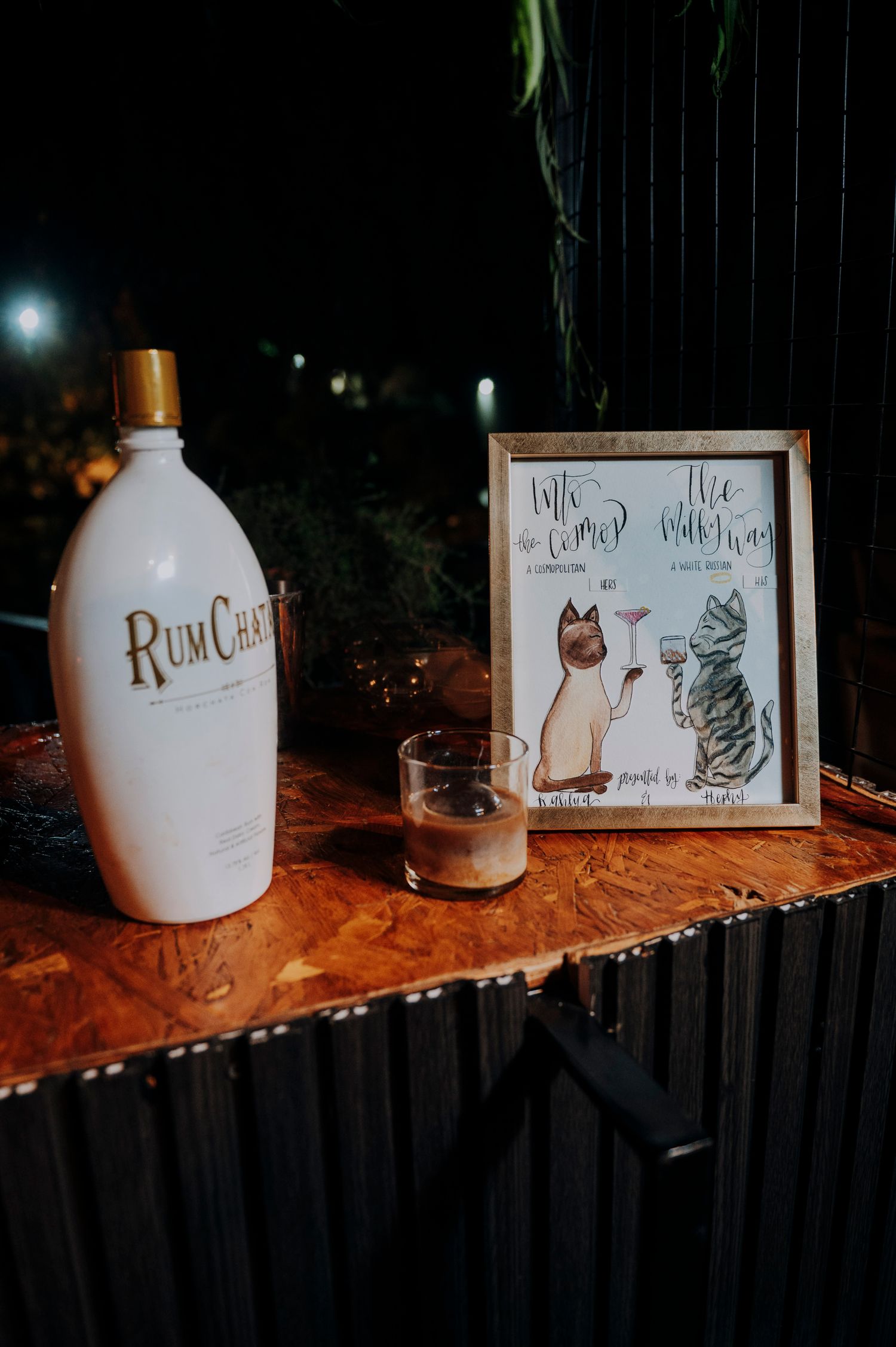 RumChata bottle and signature cocktail menu with cat illustrations displayed on bar at wedding reception.