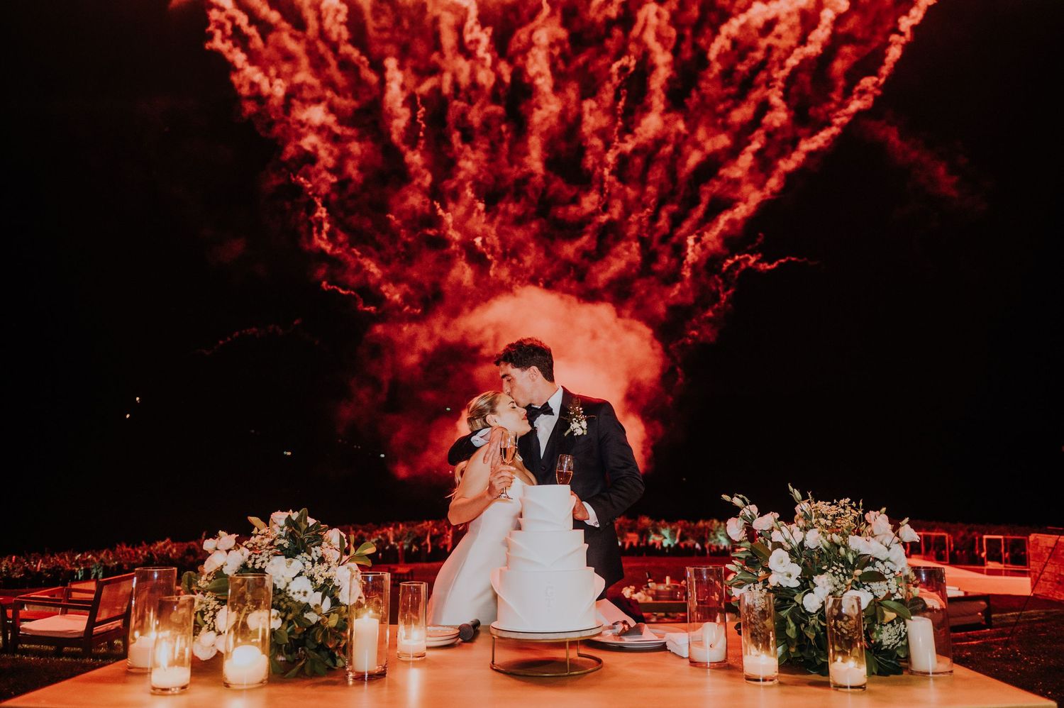 Bride and groom kiss at reception table with stunning red fireworks display overhead. during a destination wedding in Argentina.