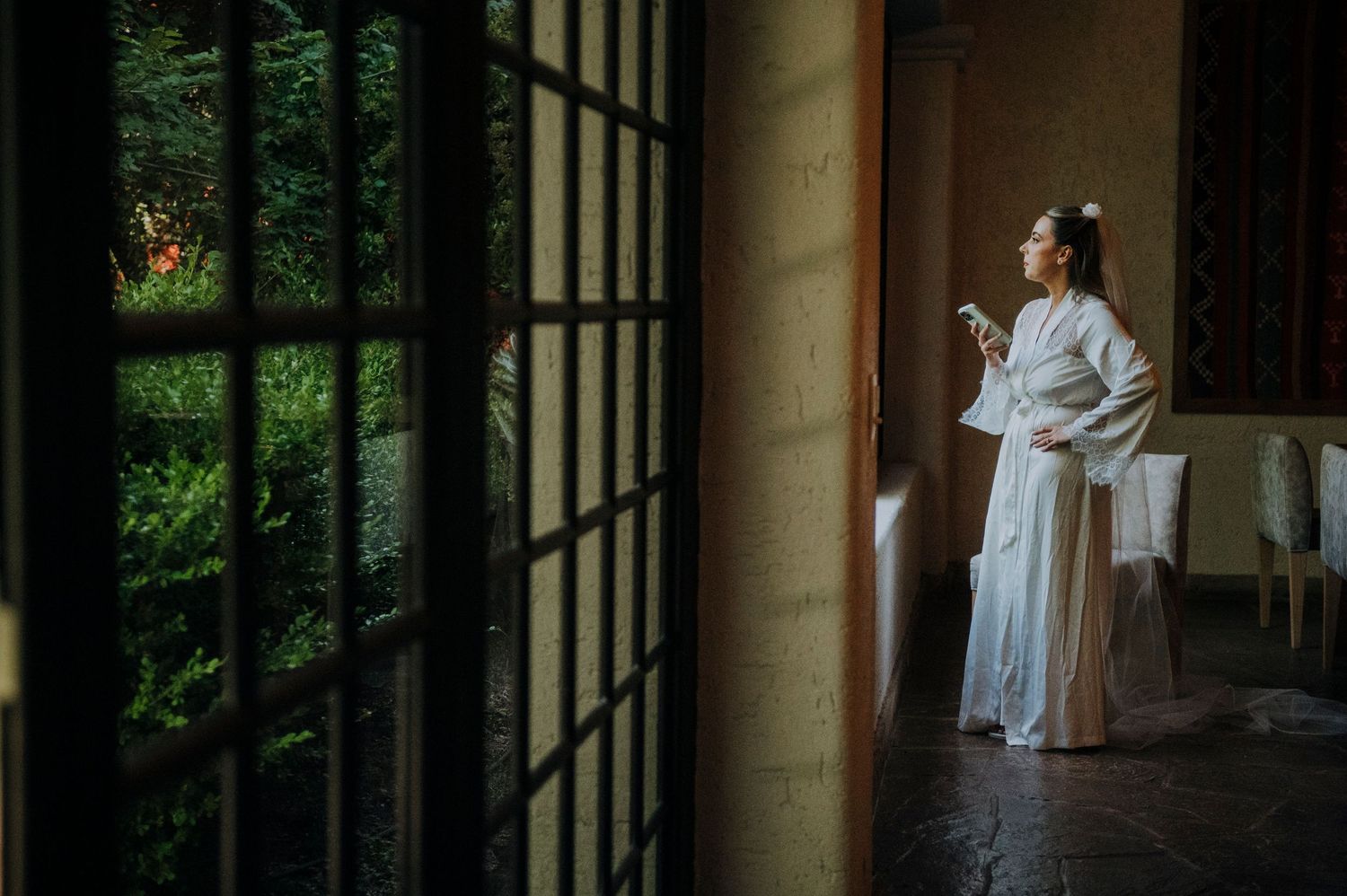 Woman in white traditional Chinese hanfu dress standing by a shoji screen door holding a phone.