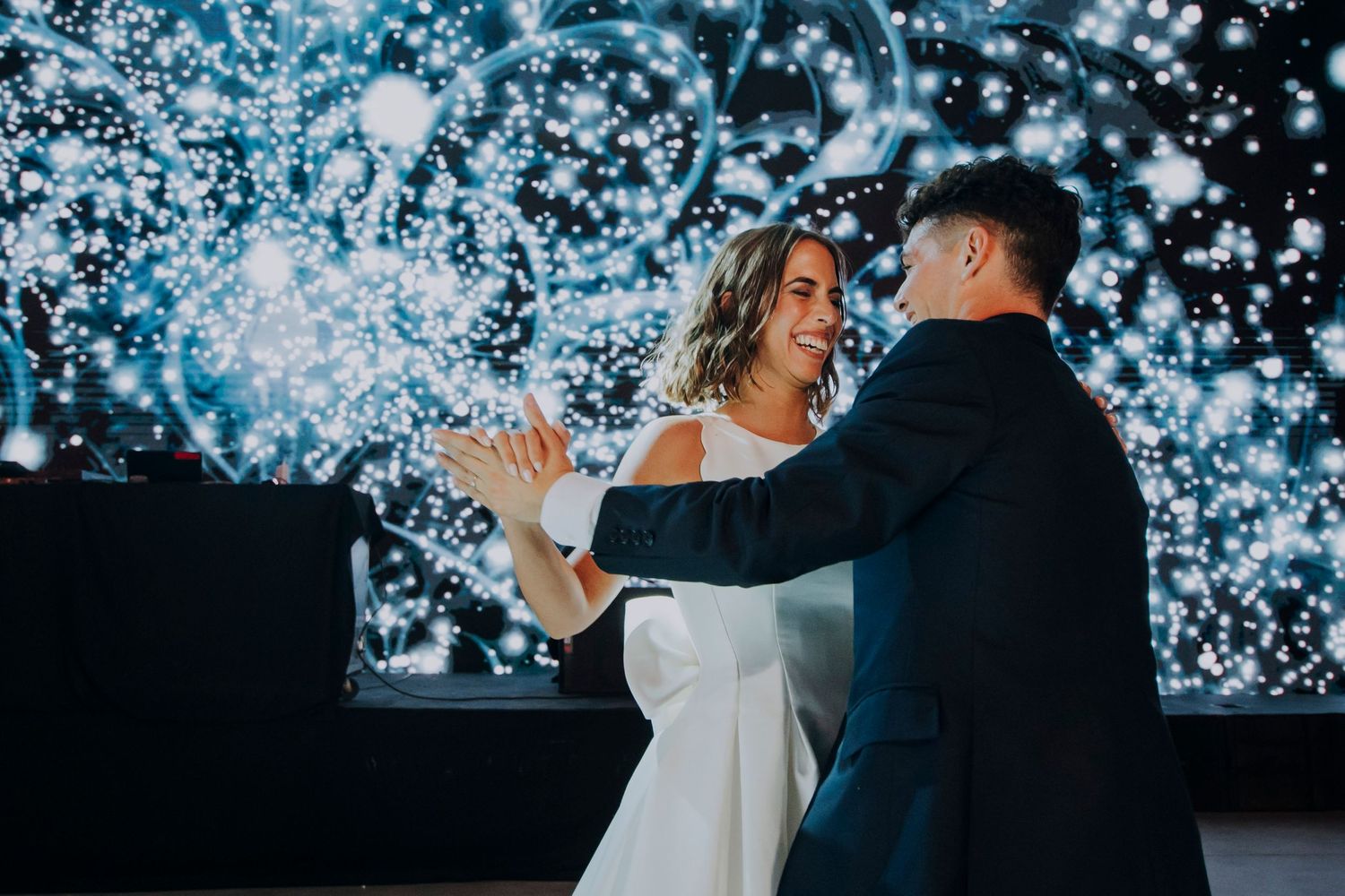 Bride and groom share their first dance in front of a stunning sparkling light display backdrop.
