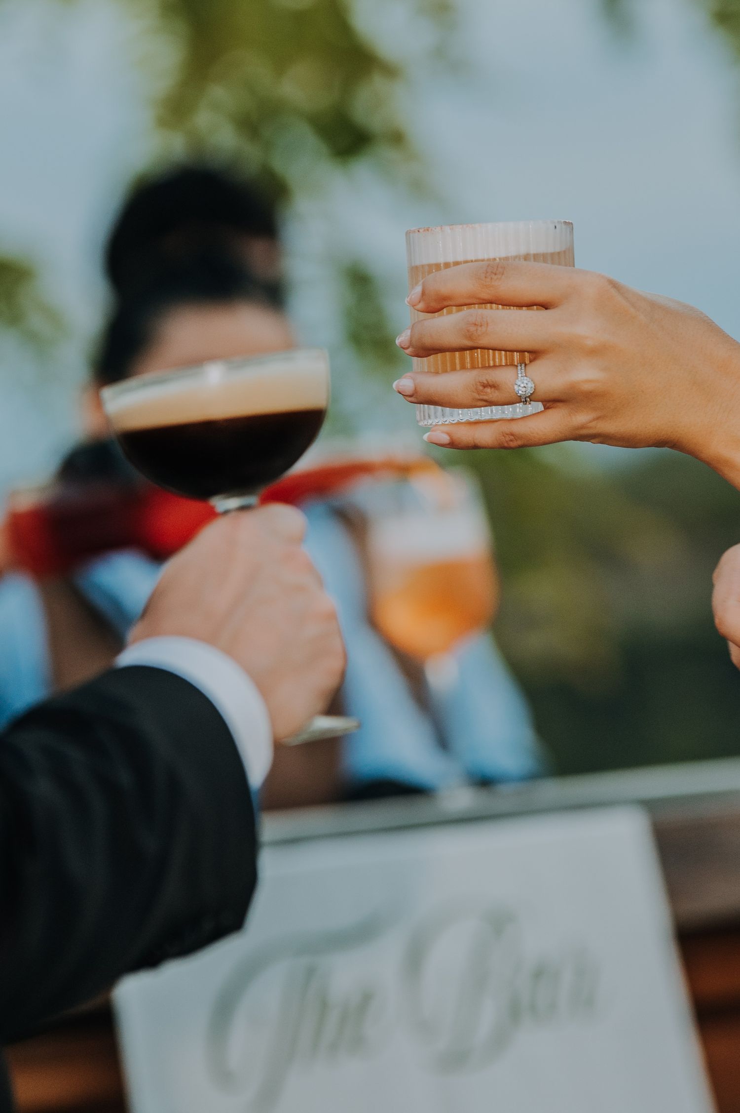 Guests clinking glasses at a wedding bar, featuring wine, beer, and cocktails with a diamond engagement ring visible.