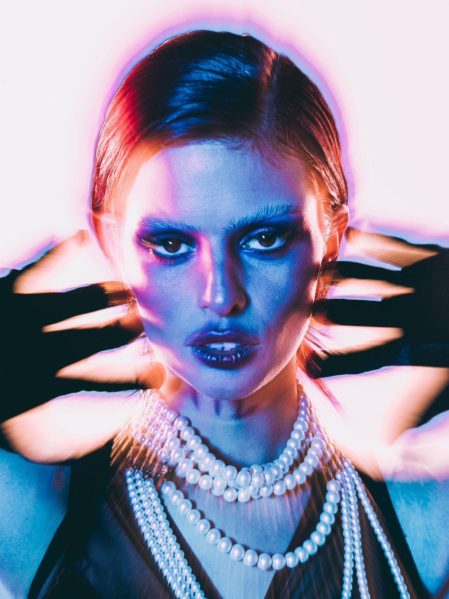 Mayra Ballesteros Fashion portrait of a woman with dramatic makeup, pearl necklaces, and blue-purple neon lighting.