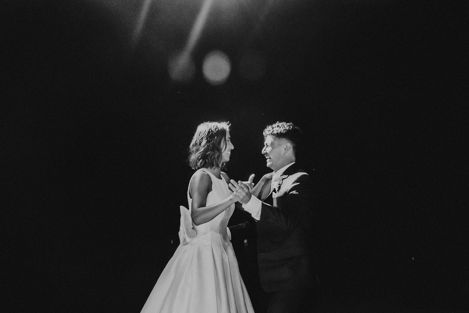Black and white photo of bride and groom sharing an intimate moment on a dramatic dark stage.