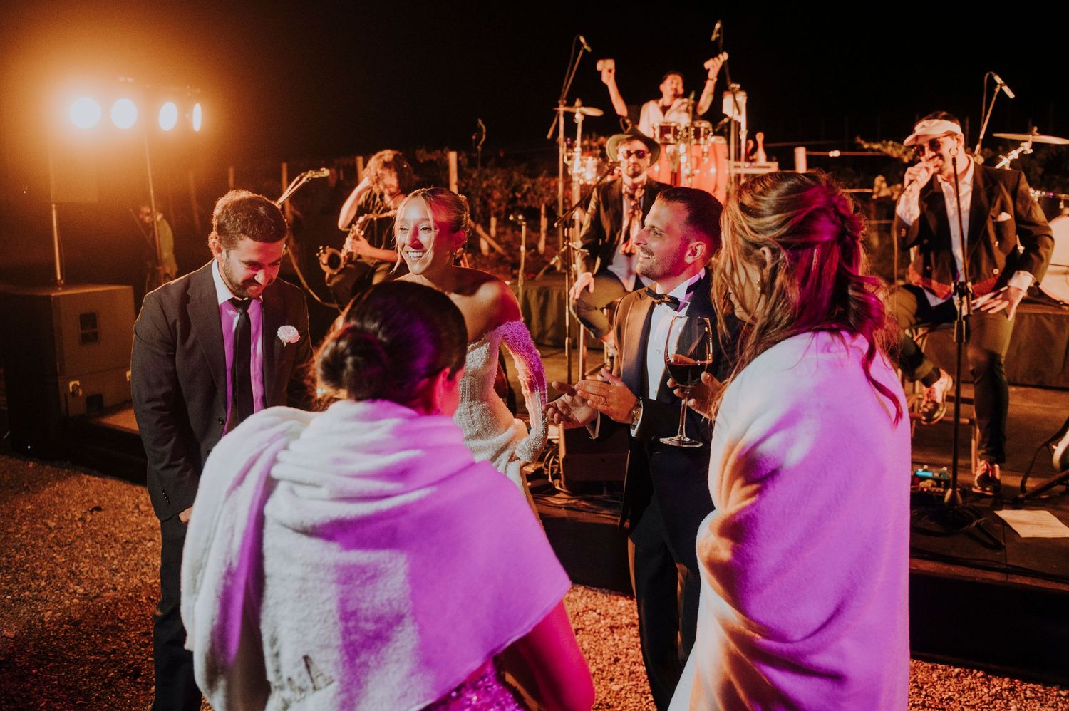 Guests dancing at an outdoor wedding reception with a live band performing on stage under warm night lights.