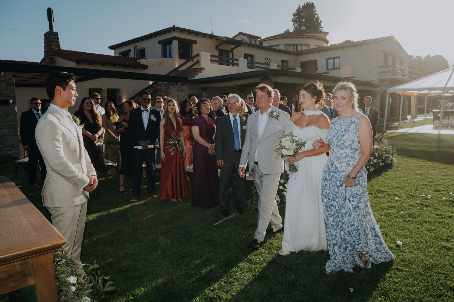 Bride and groom meet at altar during outdoor wedding ceremony with guests watching.